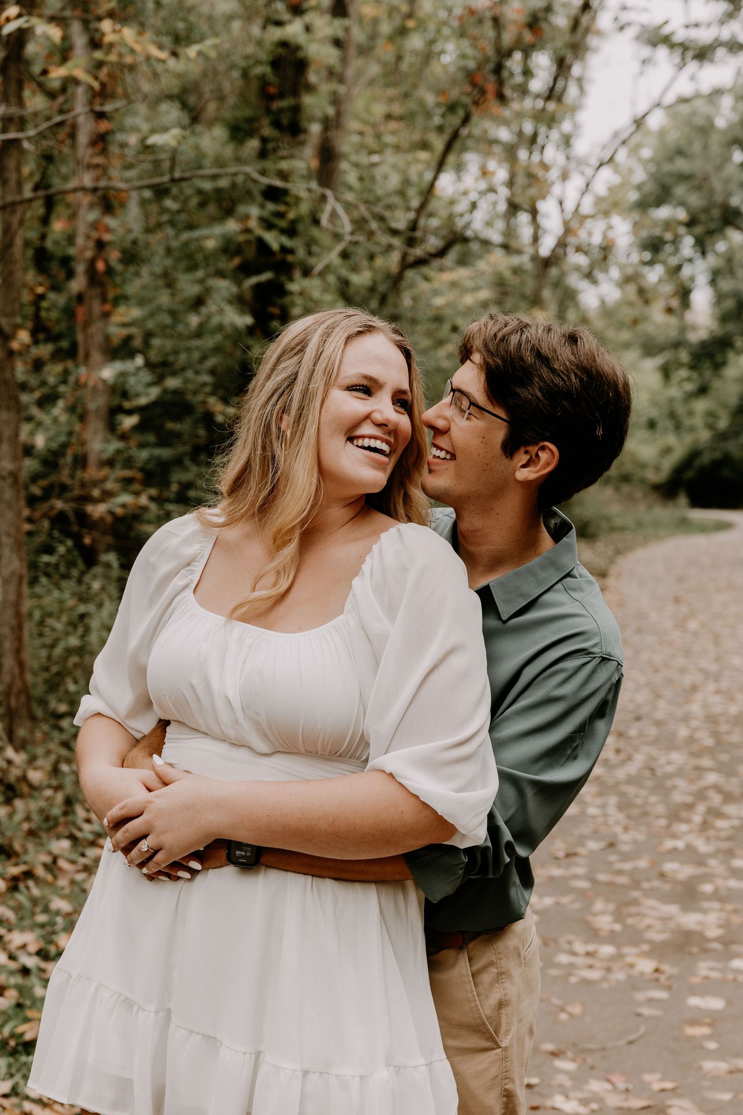 Joyful couple laughing together during outdoor engagement photo session on autumn path.