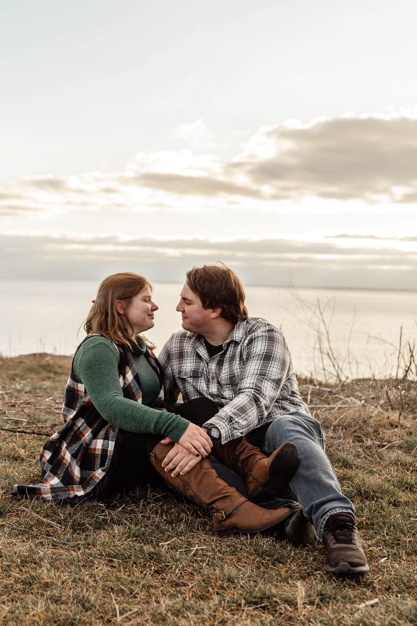 A couple in plaid shirts sits together on grass during golden hour.