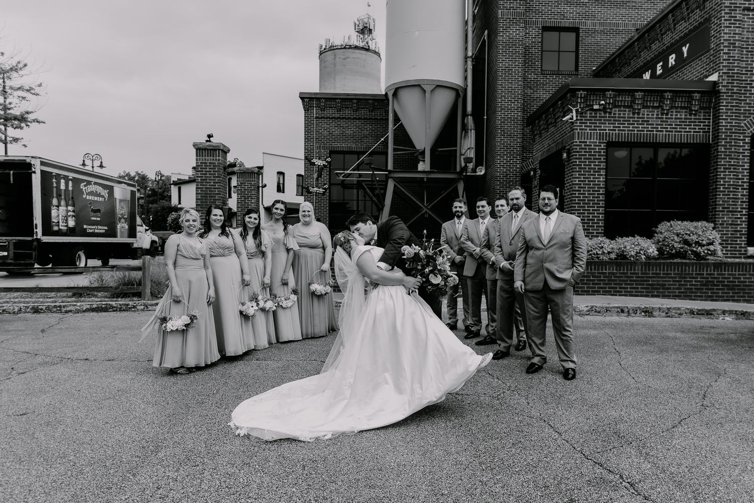 Wedding party poses in formal attire outside venue in classic black and white photography.