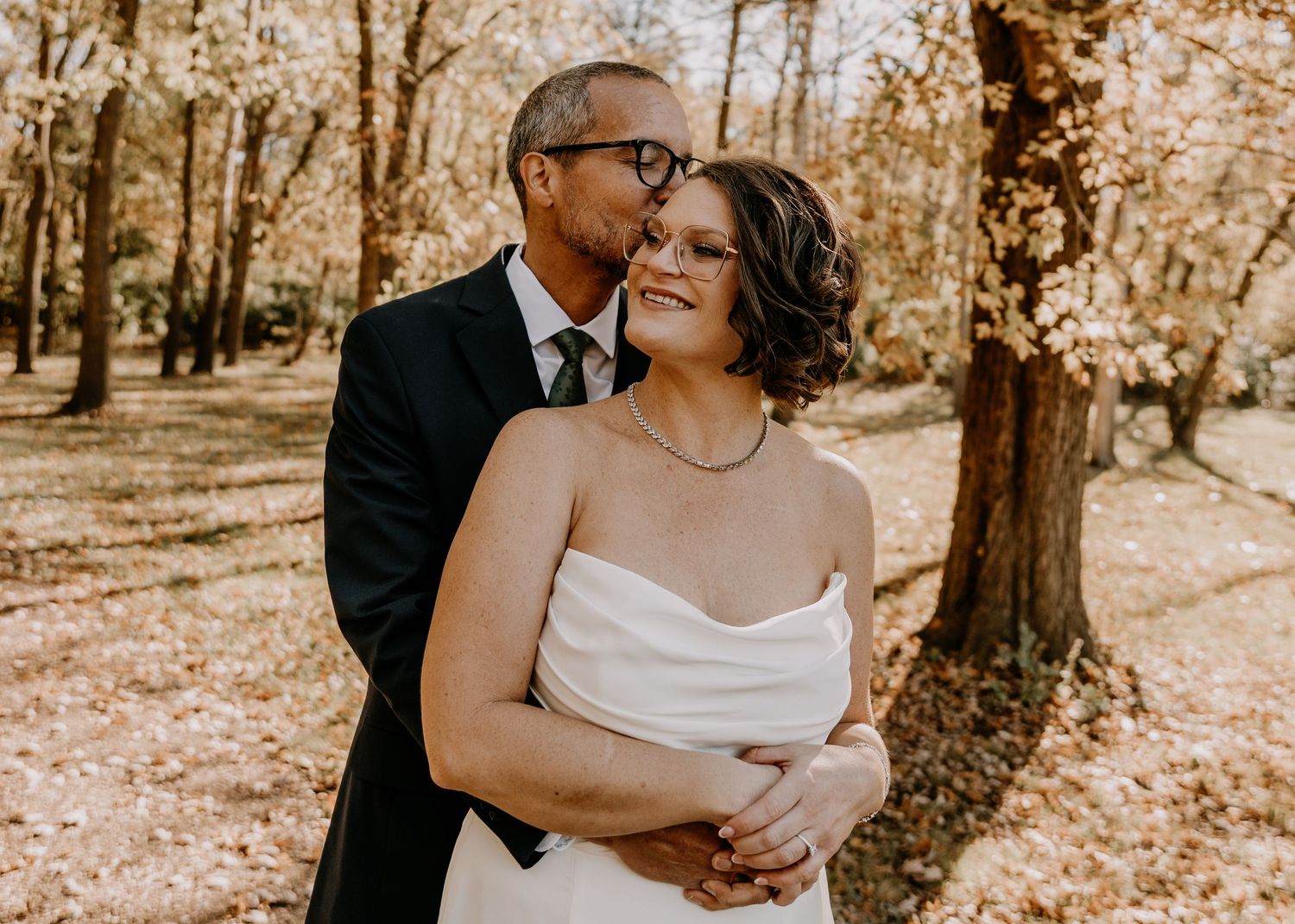 A romantic couple embraces in a sepia-toned autumn forest setting during their wedding photoshoot.
