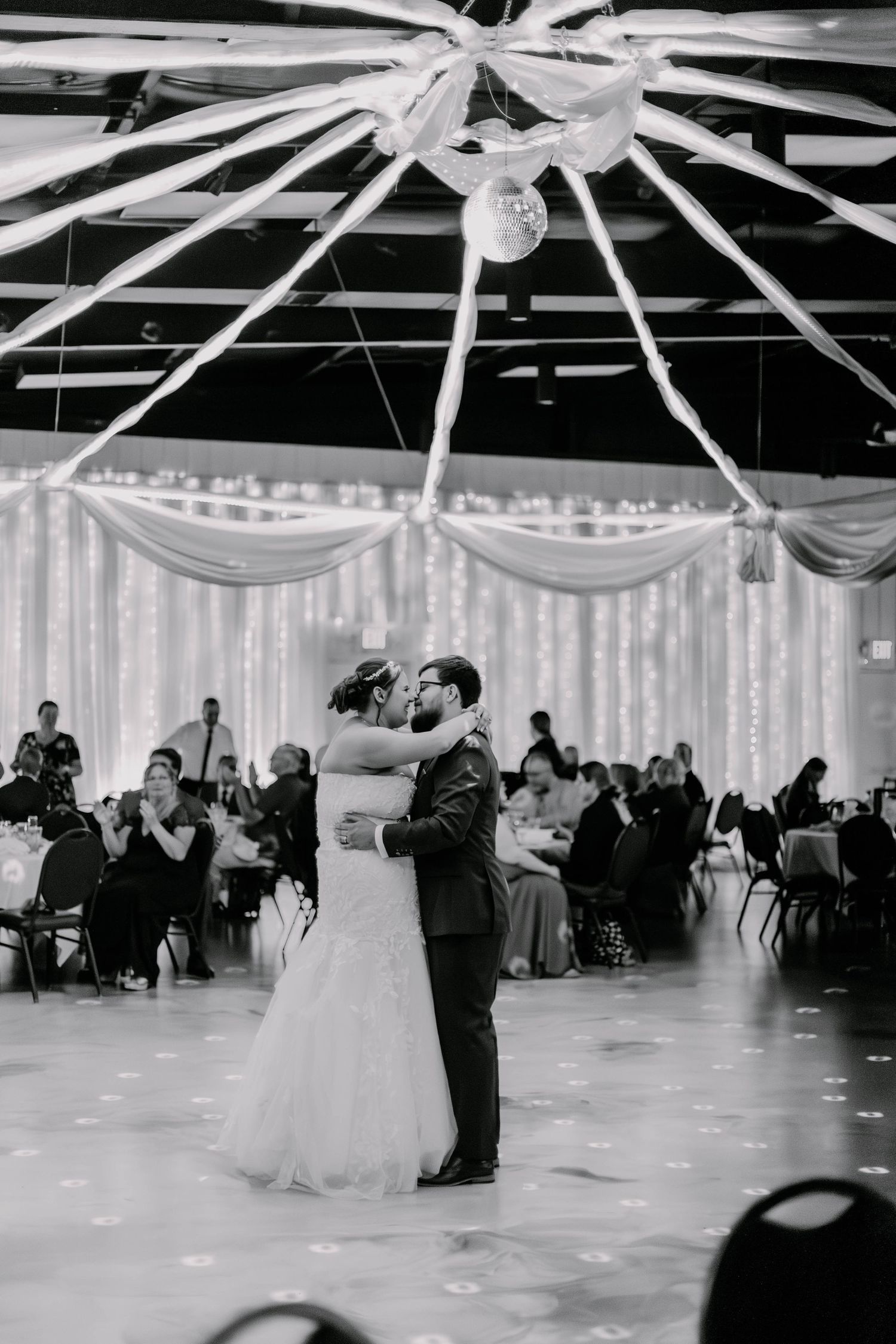 Black and white reception dance photos in decorated venue with hanging white fabric and lights.