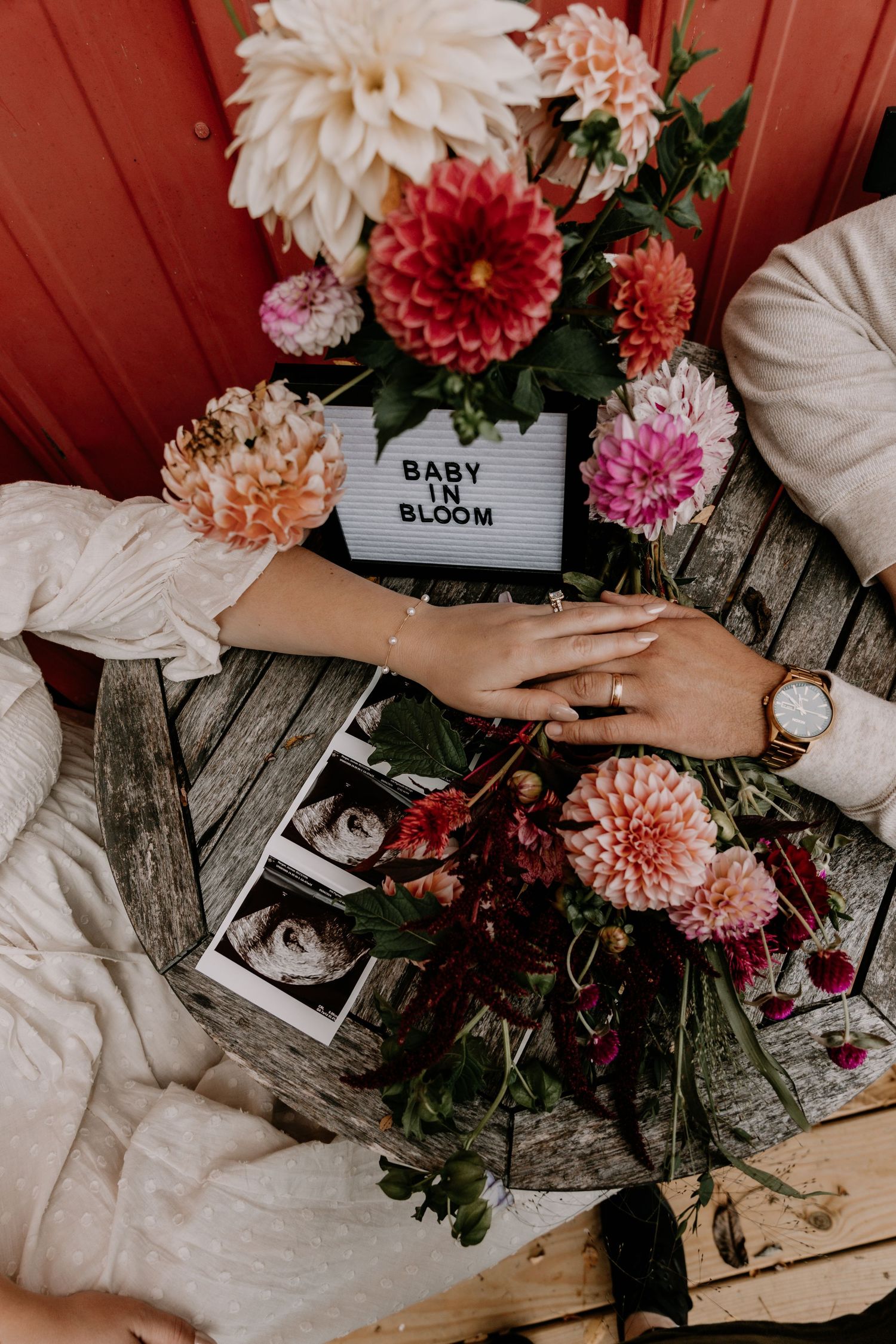 Pregnancy announcement setup with flowers and 'BABY' and 'BLOOM' signs on wooden background.