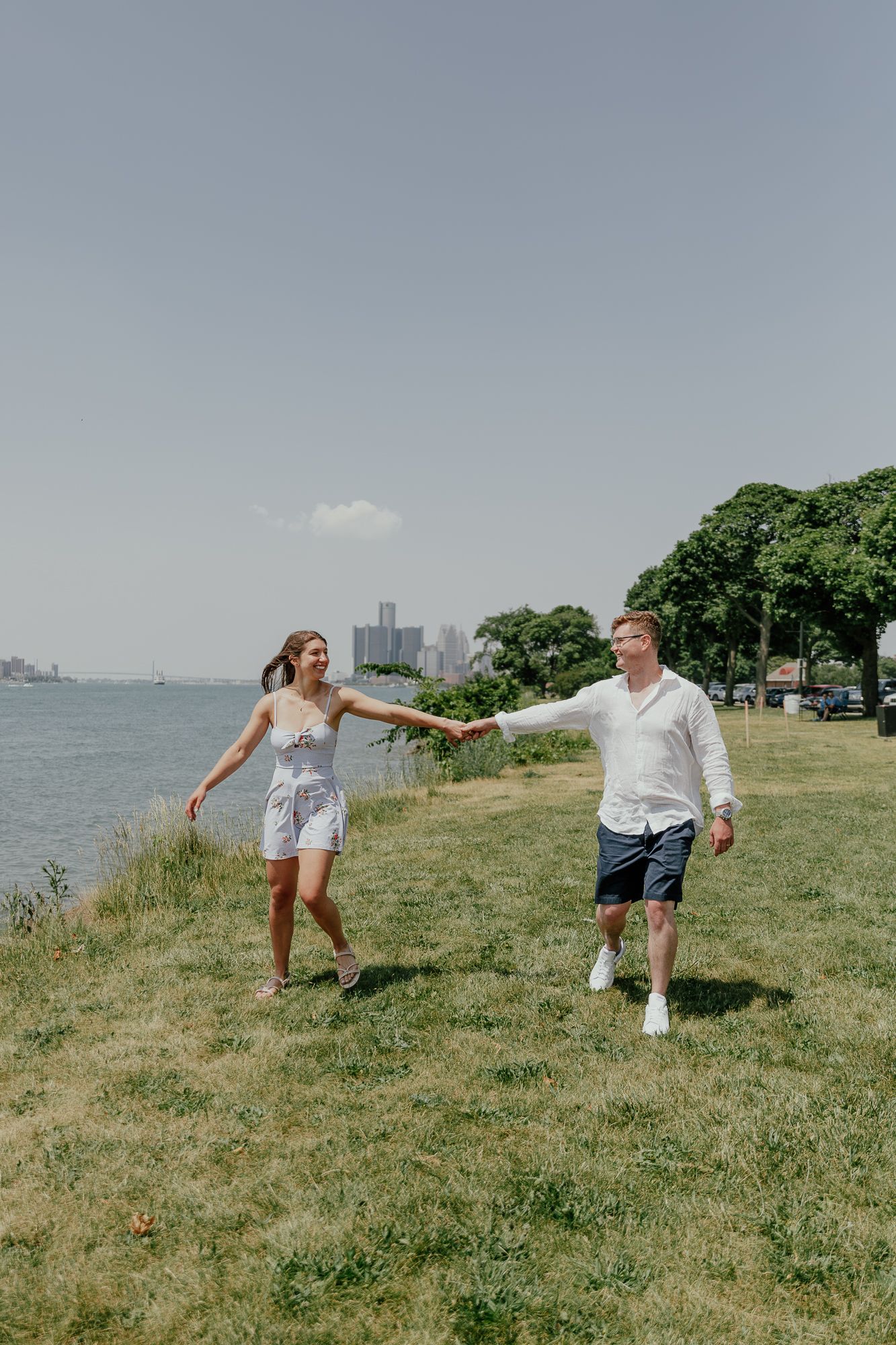 Playful couple holding hands while walking by the waterfront on a sunny day.