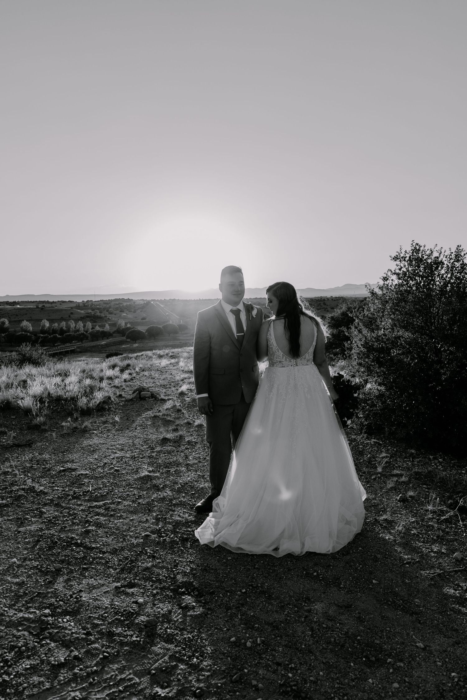 Silhouetted wedding couple walking through desert terrain at sunset.
