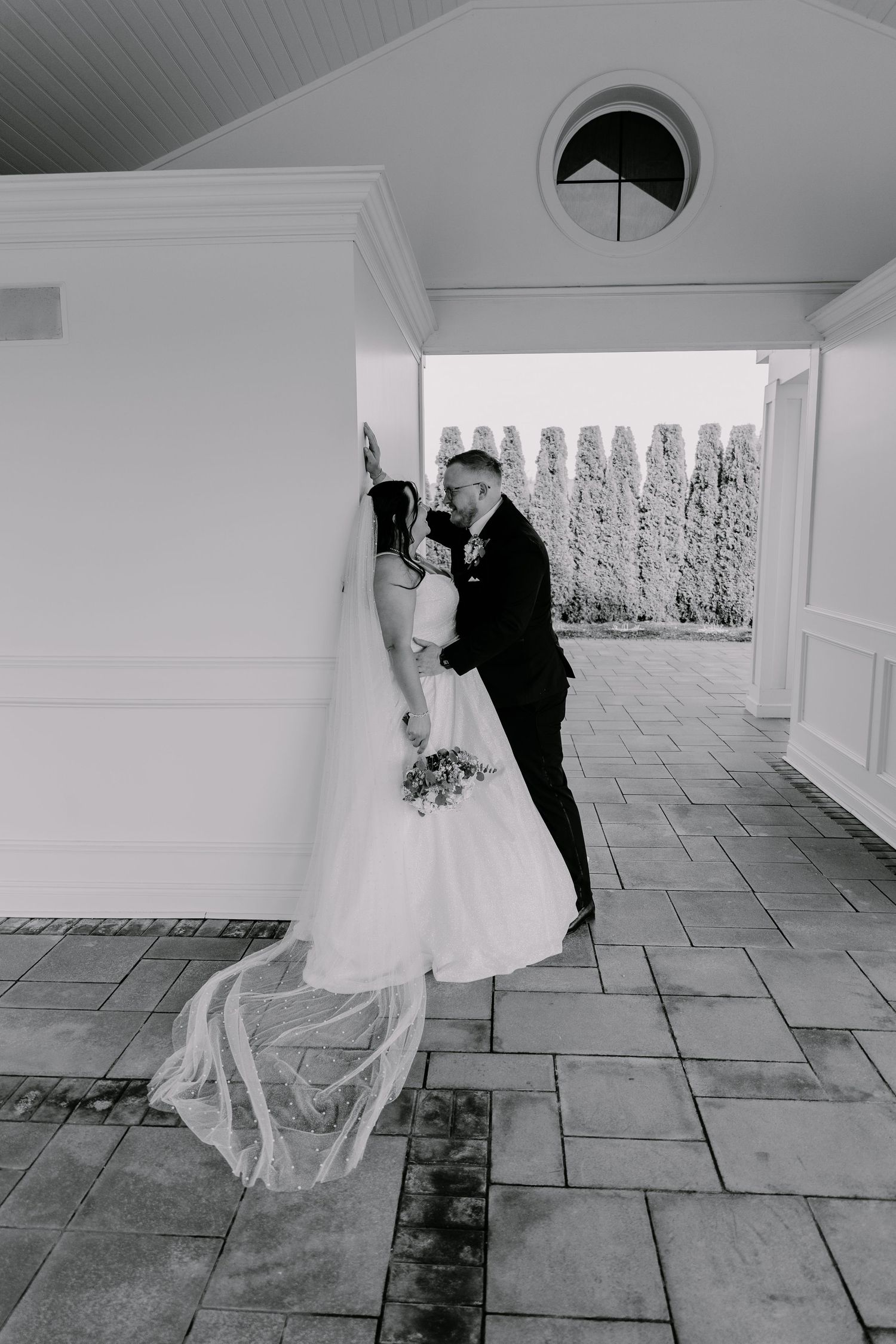 Black and white photo of a bride and groom sharing a romantic kiss under a covered patio on their wedding day.