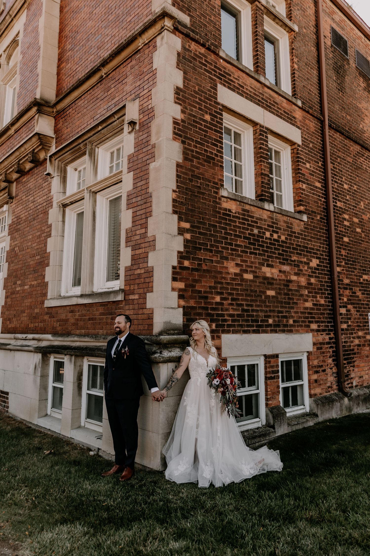 A couple takes romantic wedding photos outside a historic brick building with elegant architecture.