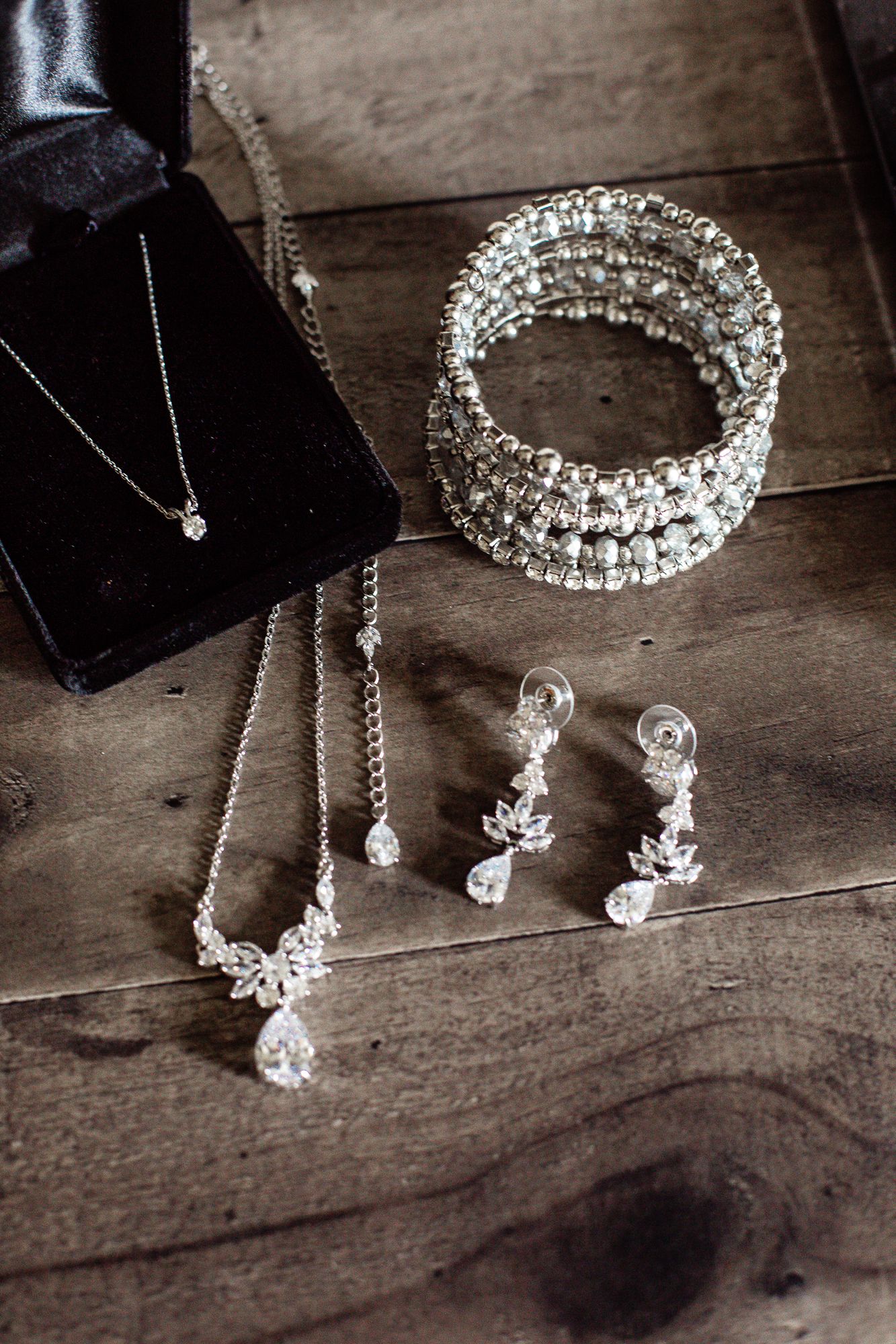 Wedding jewelry set with crystal necklace, bracelet and earrings on dark wooden surface.