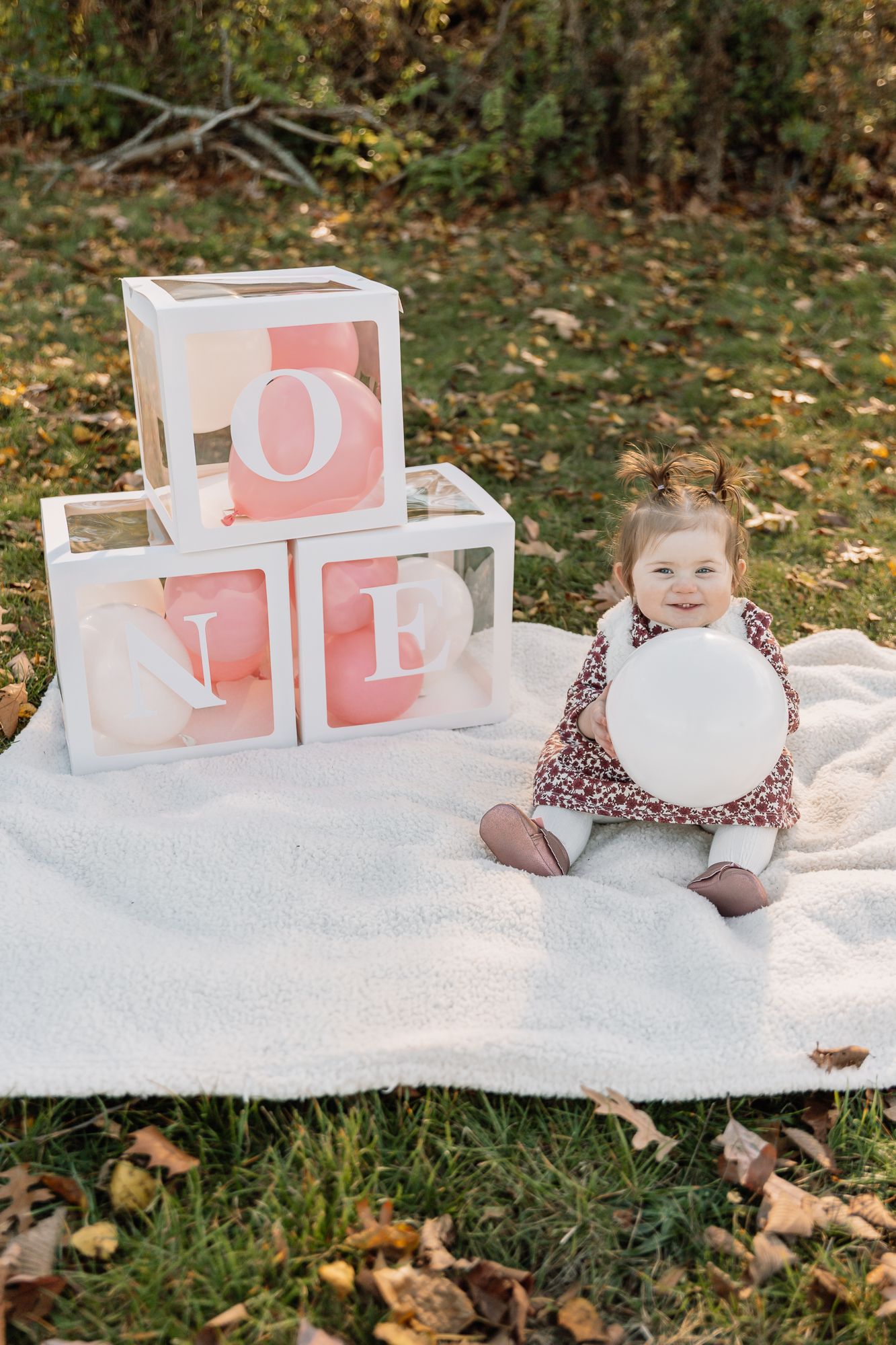 Baby sitting on white blanket with pink decorative LOVE blocks outdoors.