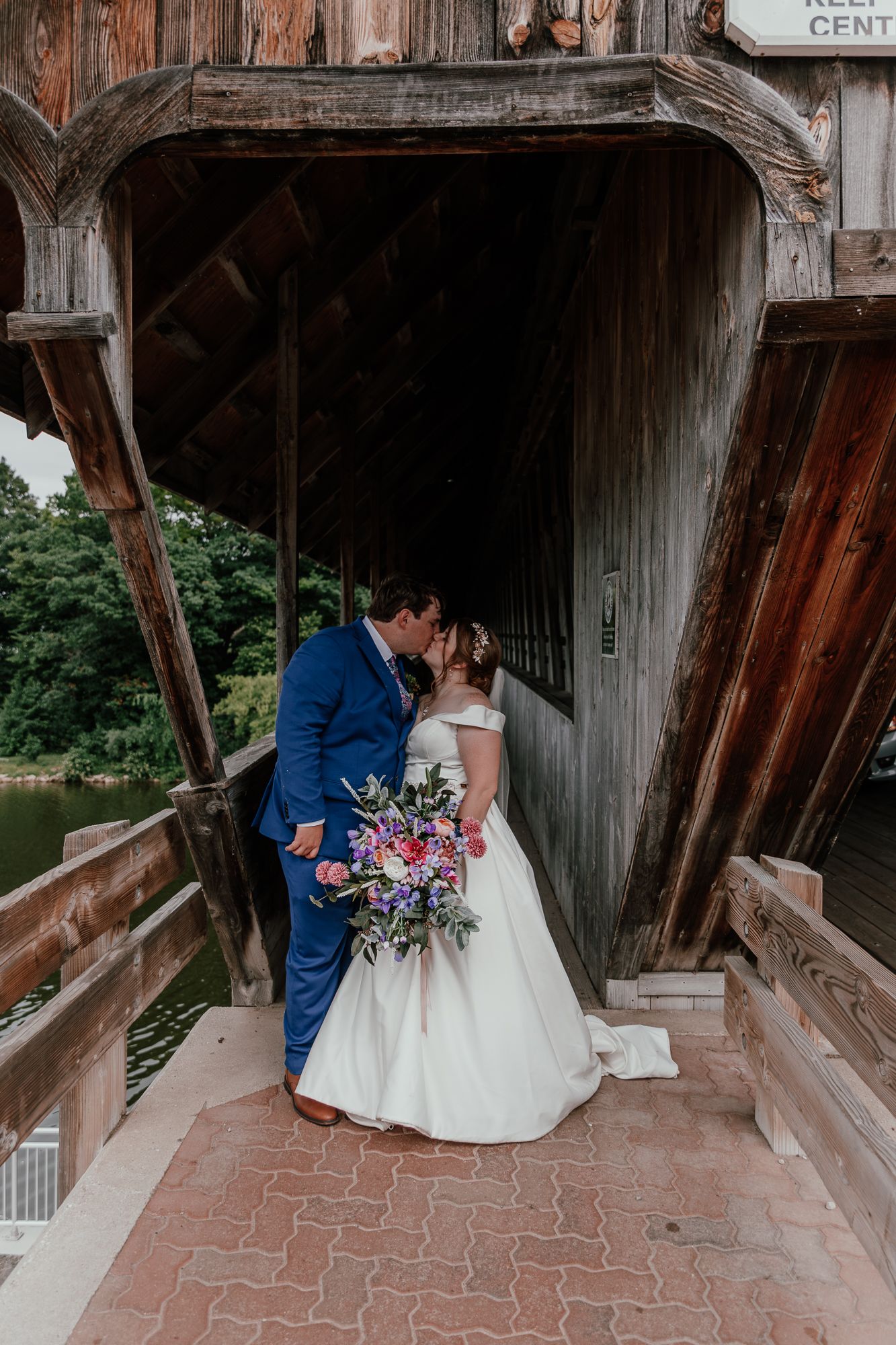 Newlyweds share intimate moment inside historic covered bridge with colorful bouquet.