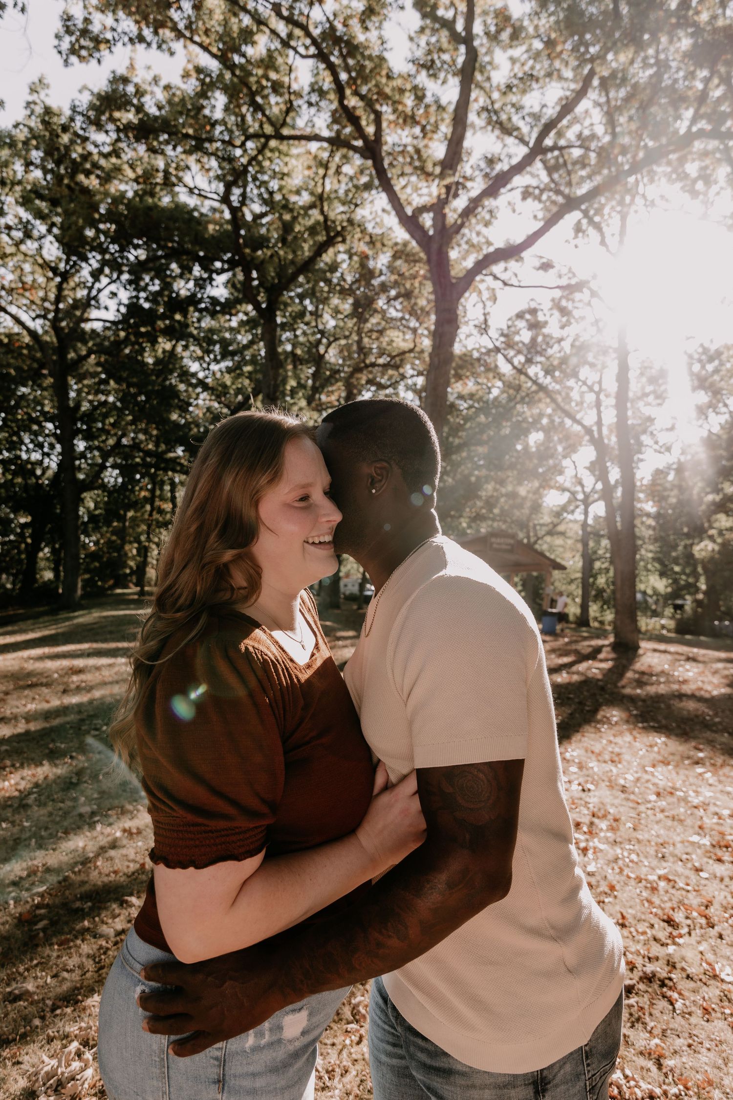 Romantic couple embraces in a sunlit autumn park setting with golden light filtering through trees.