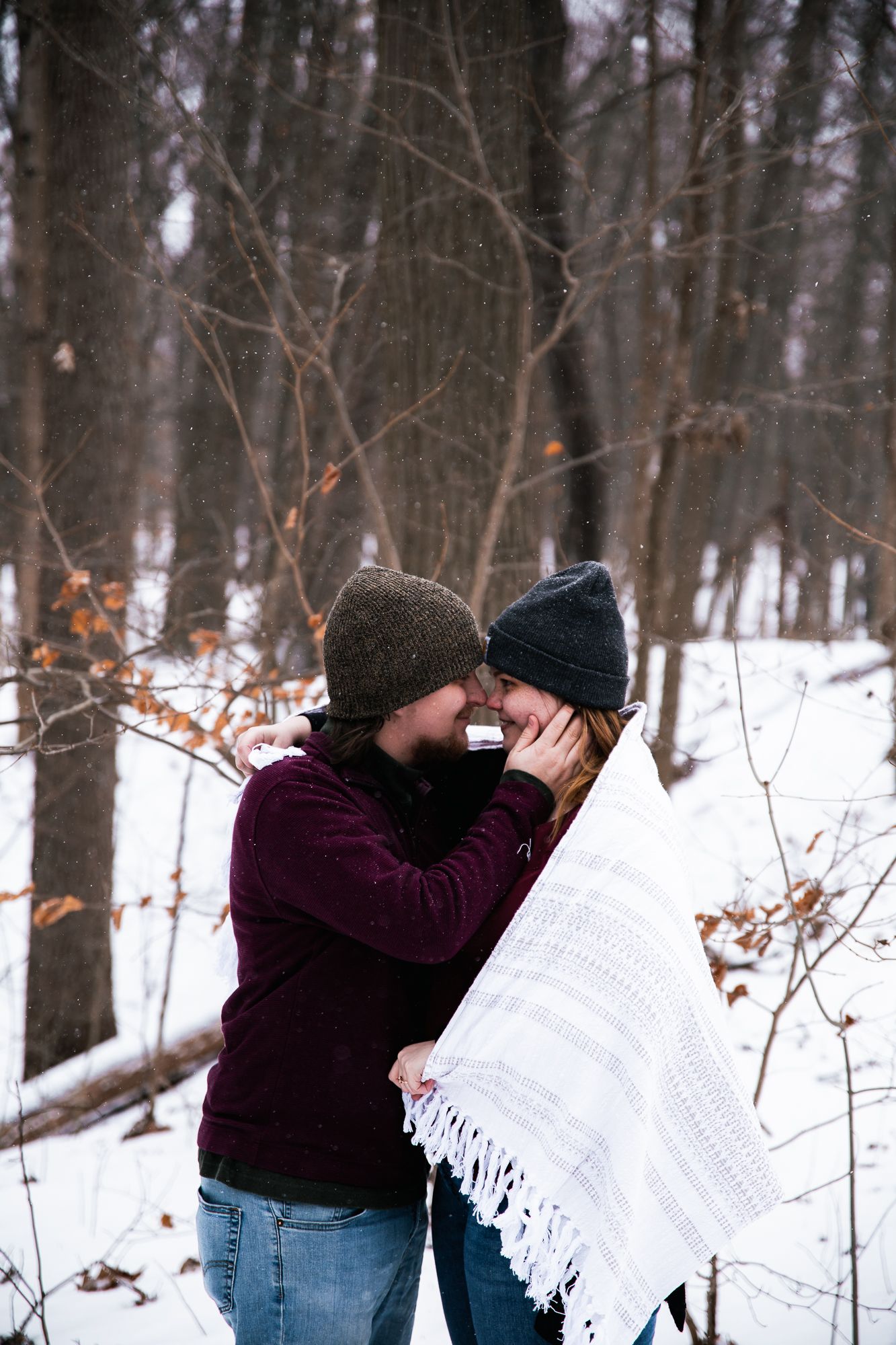 Winter forest scene with couple sharing intimate moments among snowy trees.