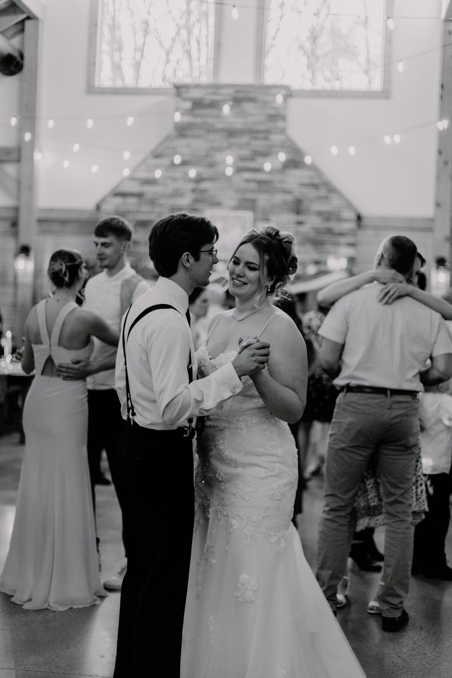 Couple dancing together during wedding reception in barn venue with stone fireplace backdrop.