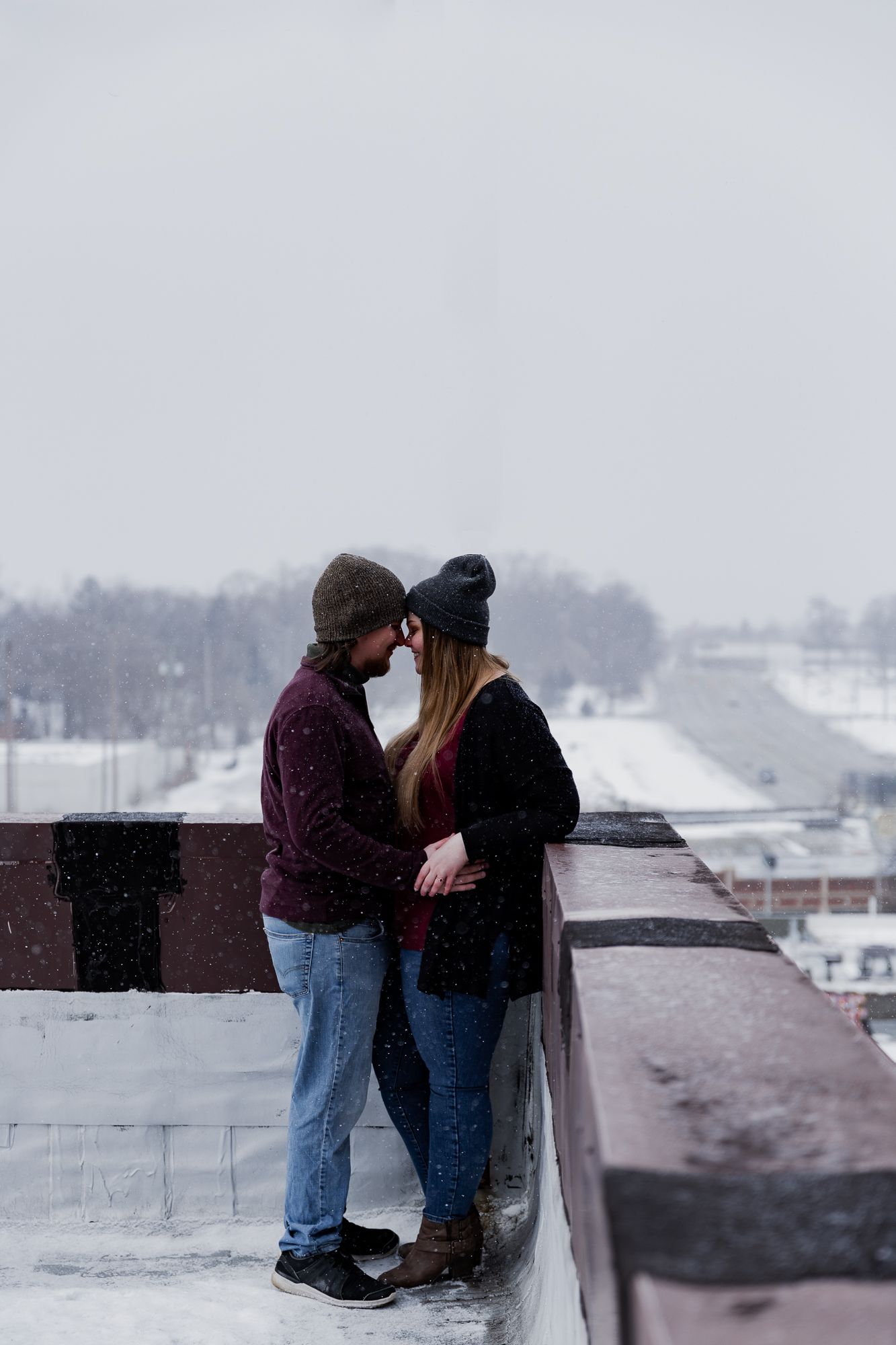 Romantic winter scene with two people embracing on a rooftop overlooking a snowy landscape.