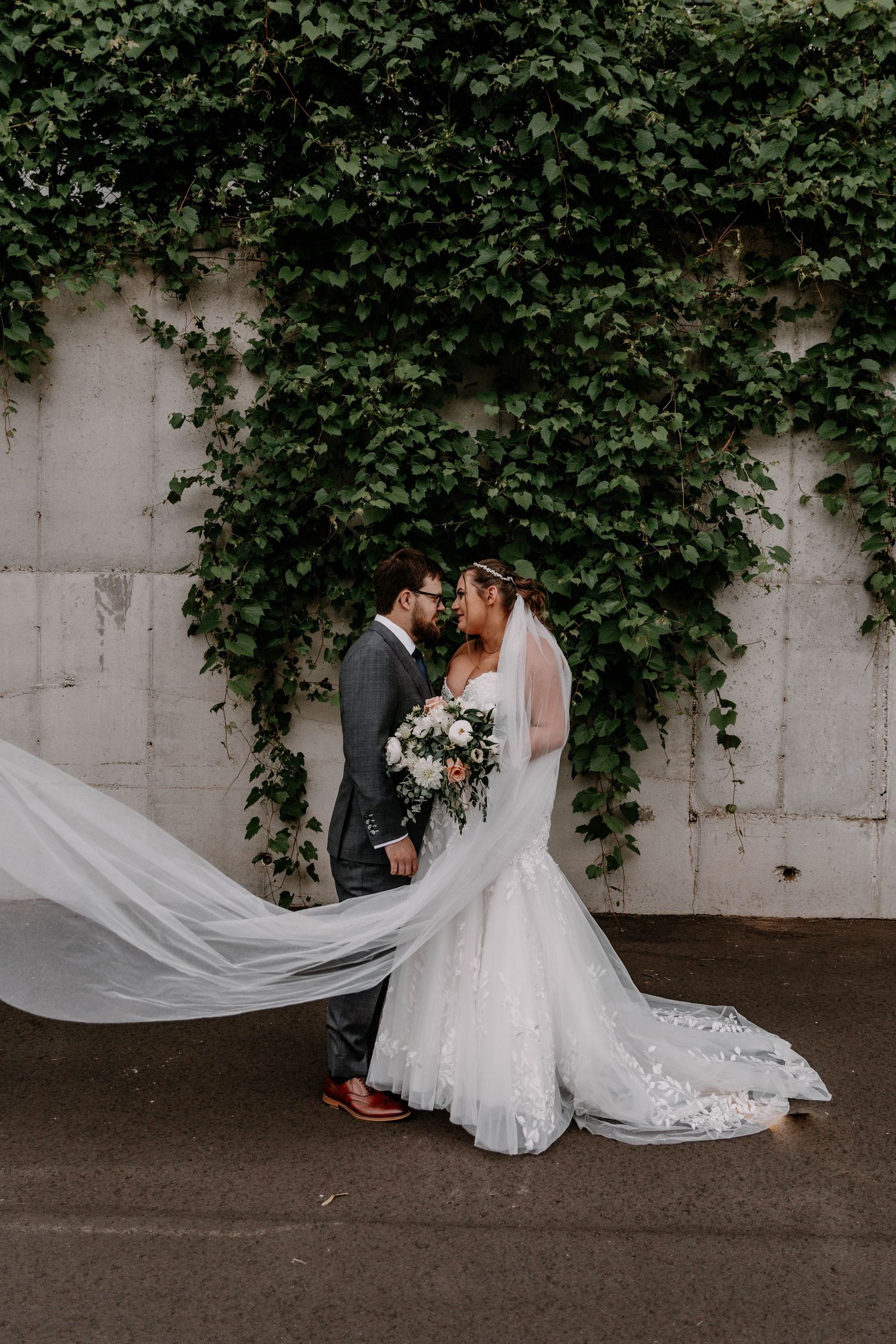 Wedding couple shares intimate moment against wall covered in lush green ivy vines.