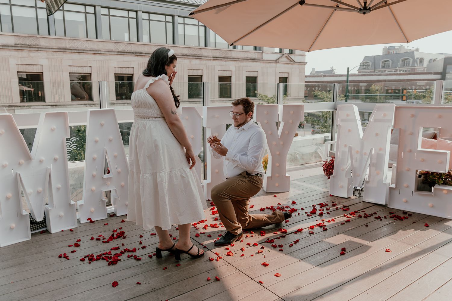 Romantic rooftop proposal scene with rose petals and white decorations.
