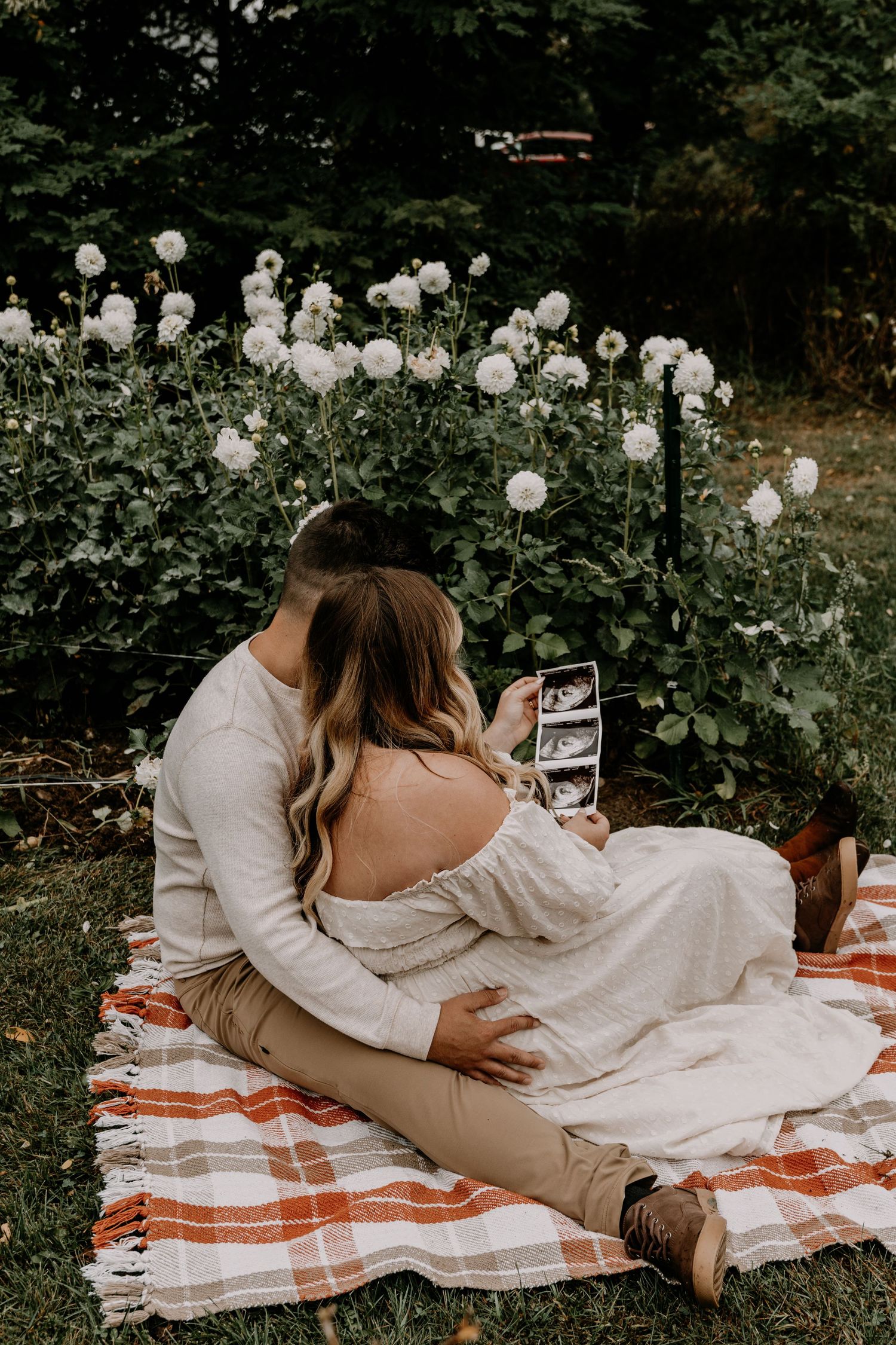 Couple relaxing on striped picnic blanket surrounded by white flowers in garden setting.