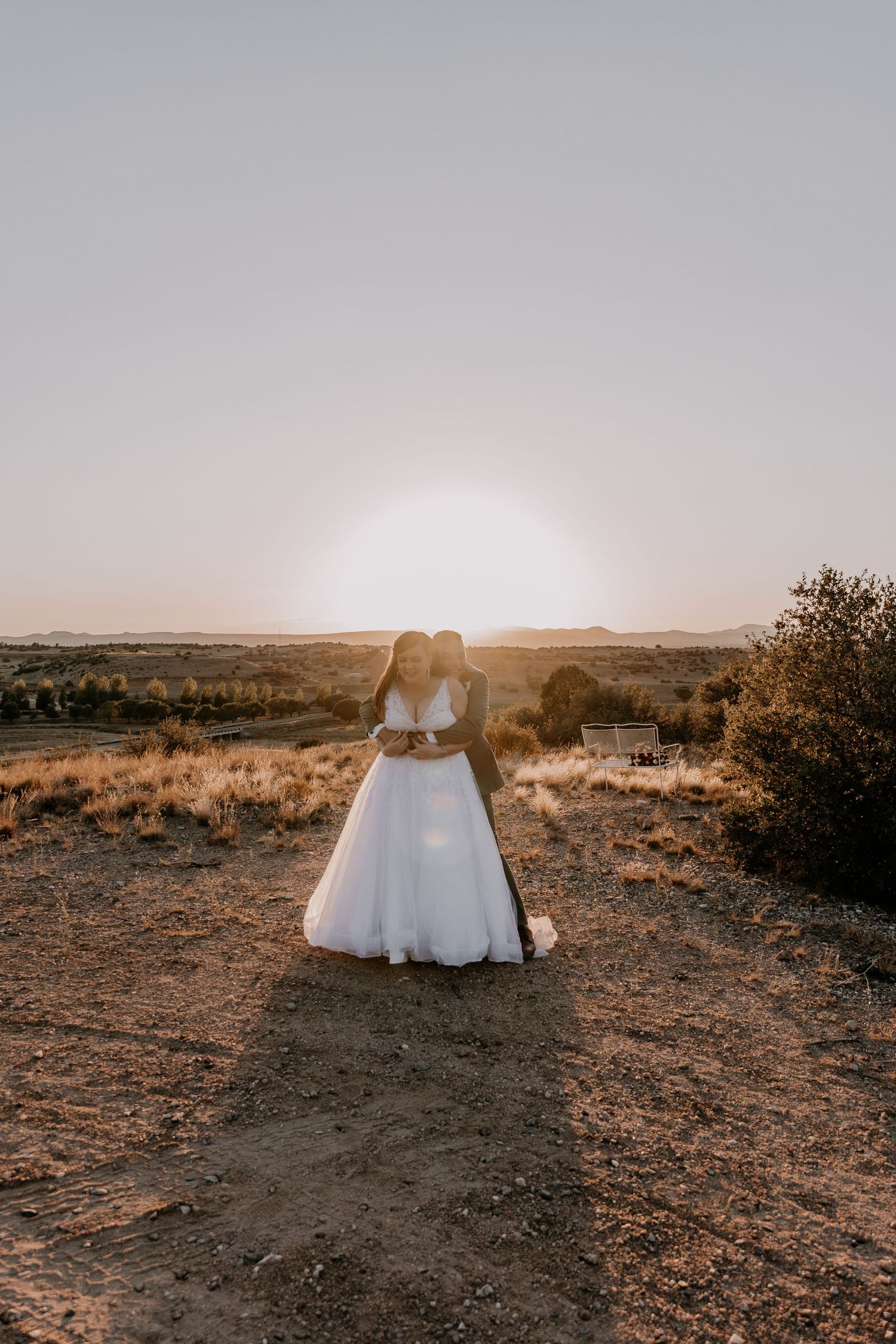 A wedding dress silhouette against a desert sunset landscape with distant mountains and sparse vegetation.
