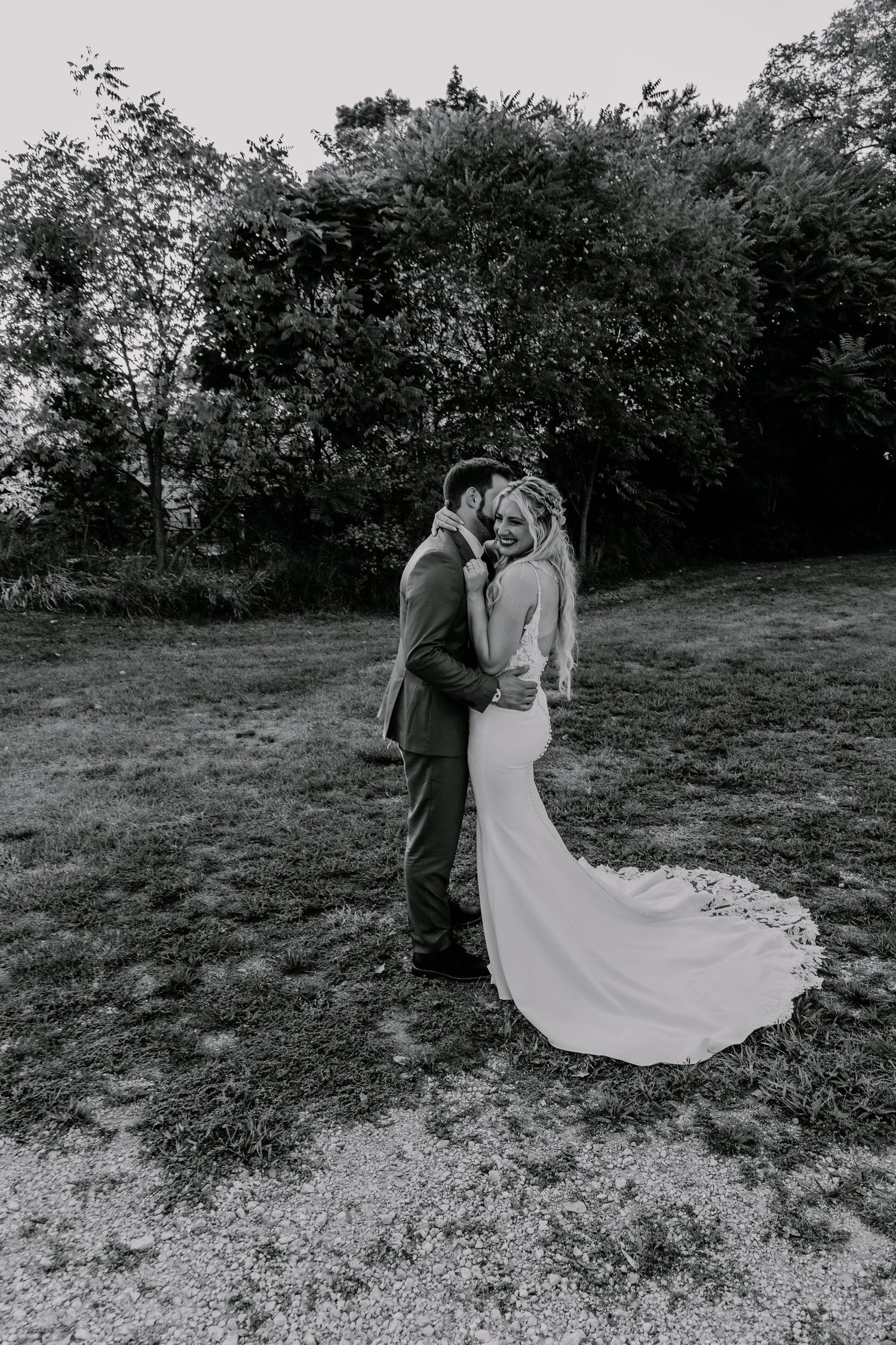 A romantic black and white wedding photo captured on a hillside with trees in the background.