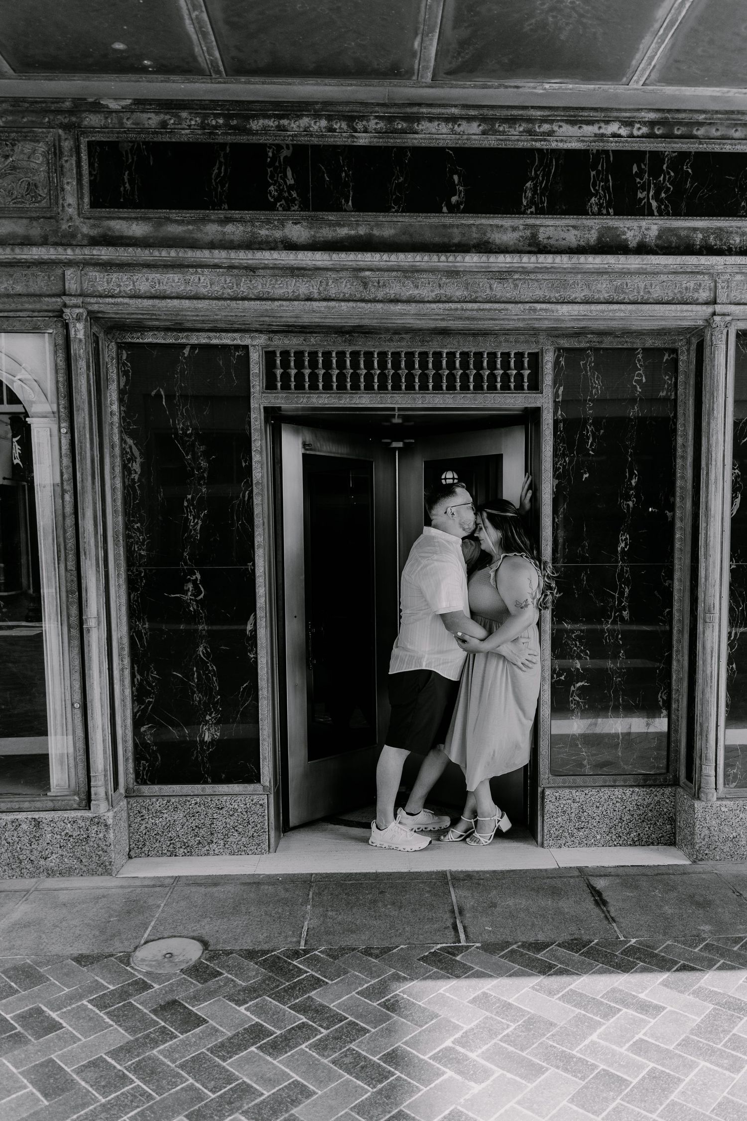 Black and white photo of couple sharing tender moment in vintage elevator doorway.