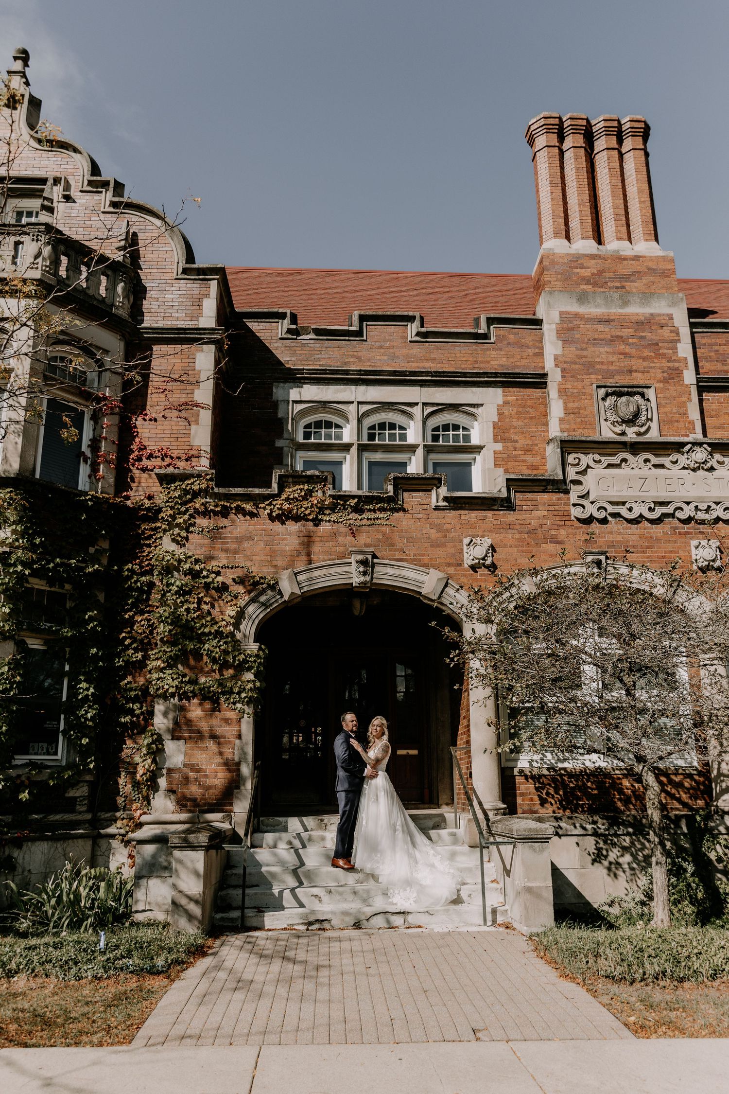 A wedding couple poses in front of a historic brick building with Gothic architectural details.