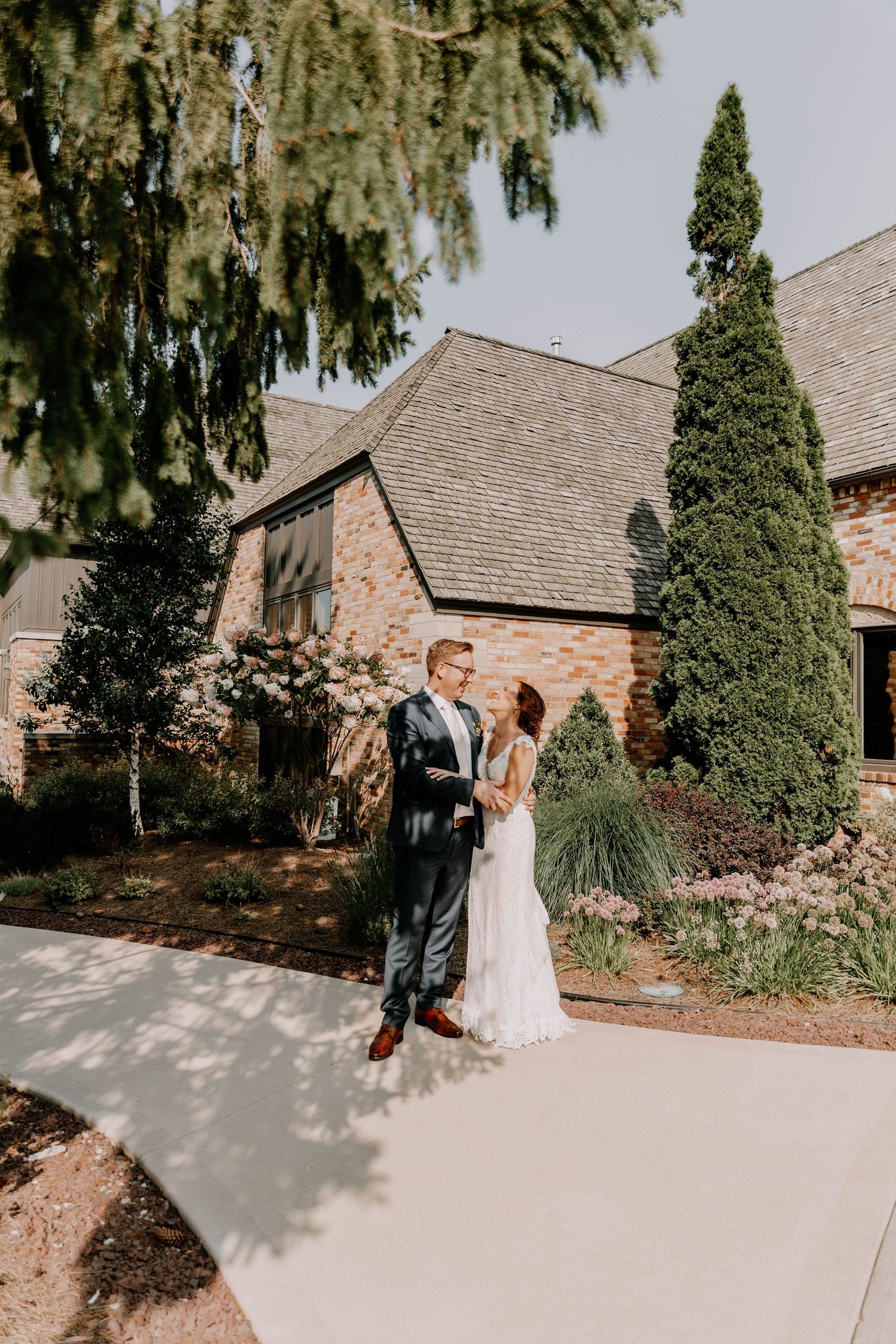 Romantic portrait of newlyweds standing outside stone church with beautiful garden landscaping.