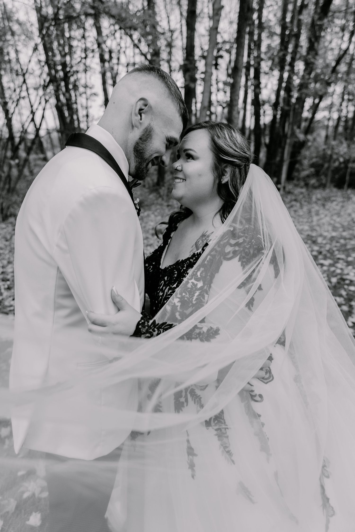 Black and white portrait of couple sharing tender moment under flowing bridal veil.
