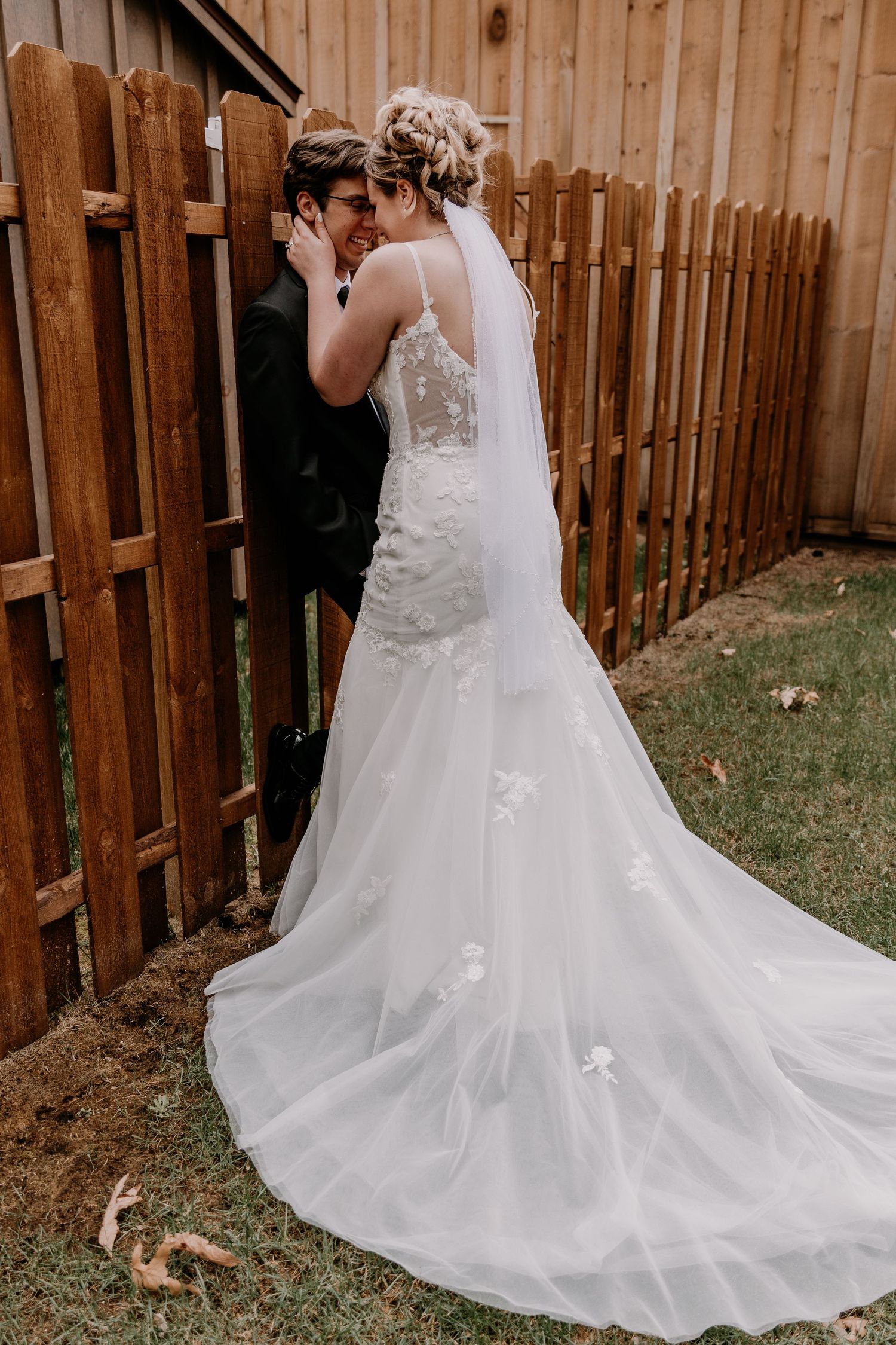 Beautiful flowing white wedding dress with lace details and long train against wooden fence.