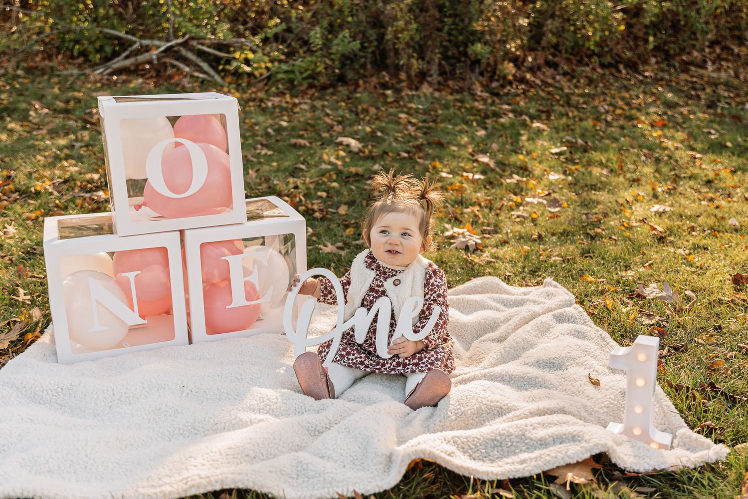 Toddler sitting on blanket with pink letter blocks during outdoor photo session.