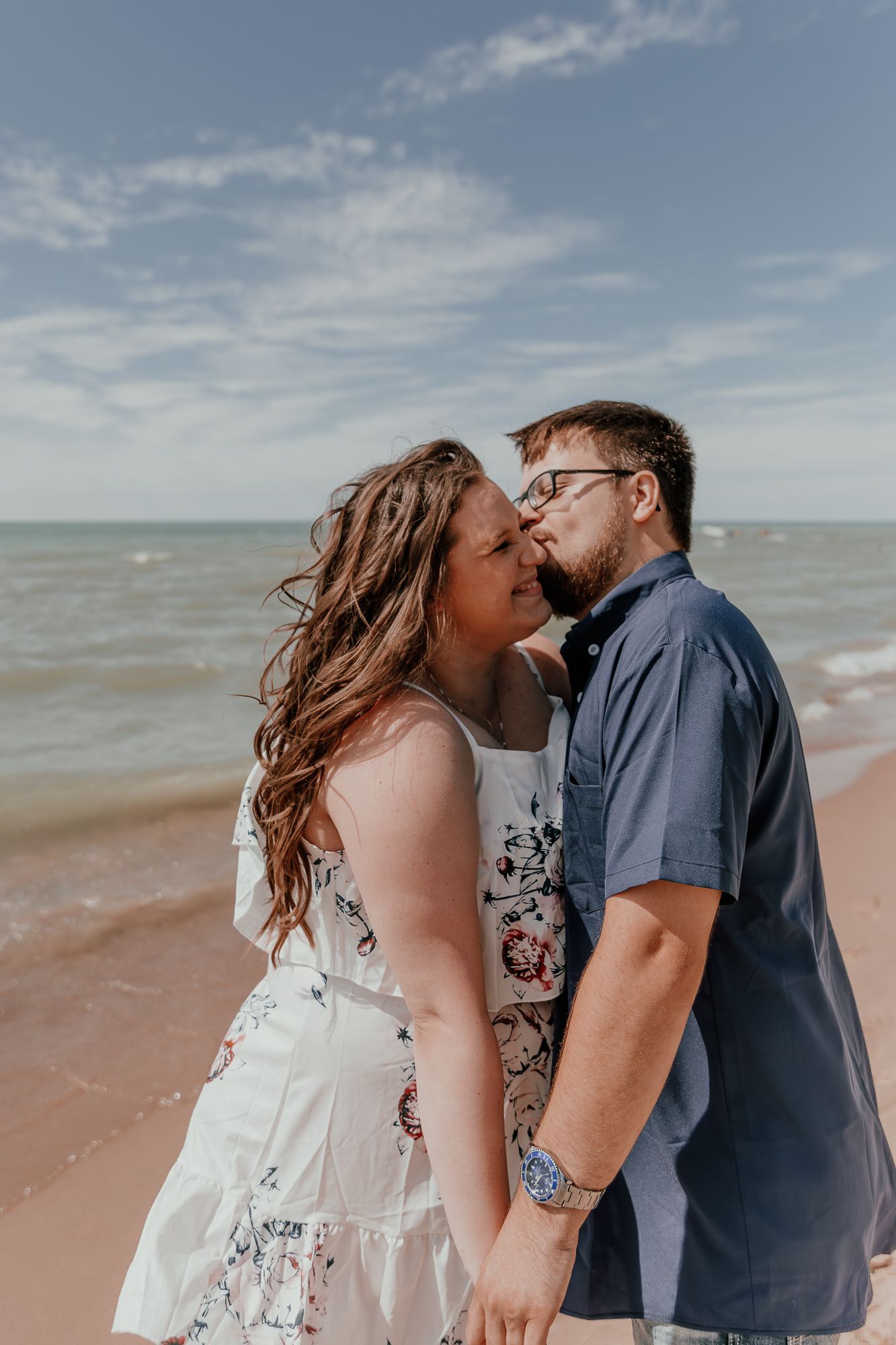 Intimate moment between couple on sunny beach with waves crashing in background.