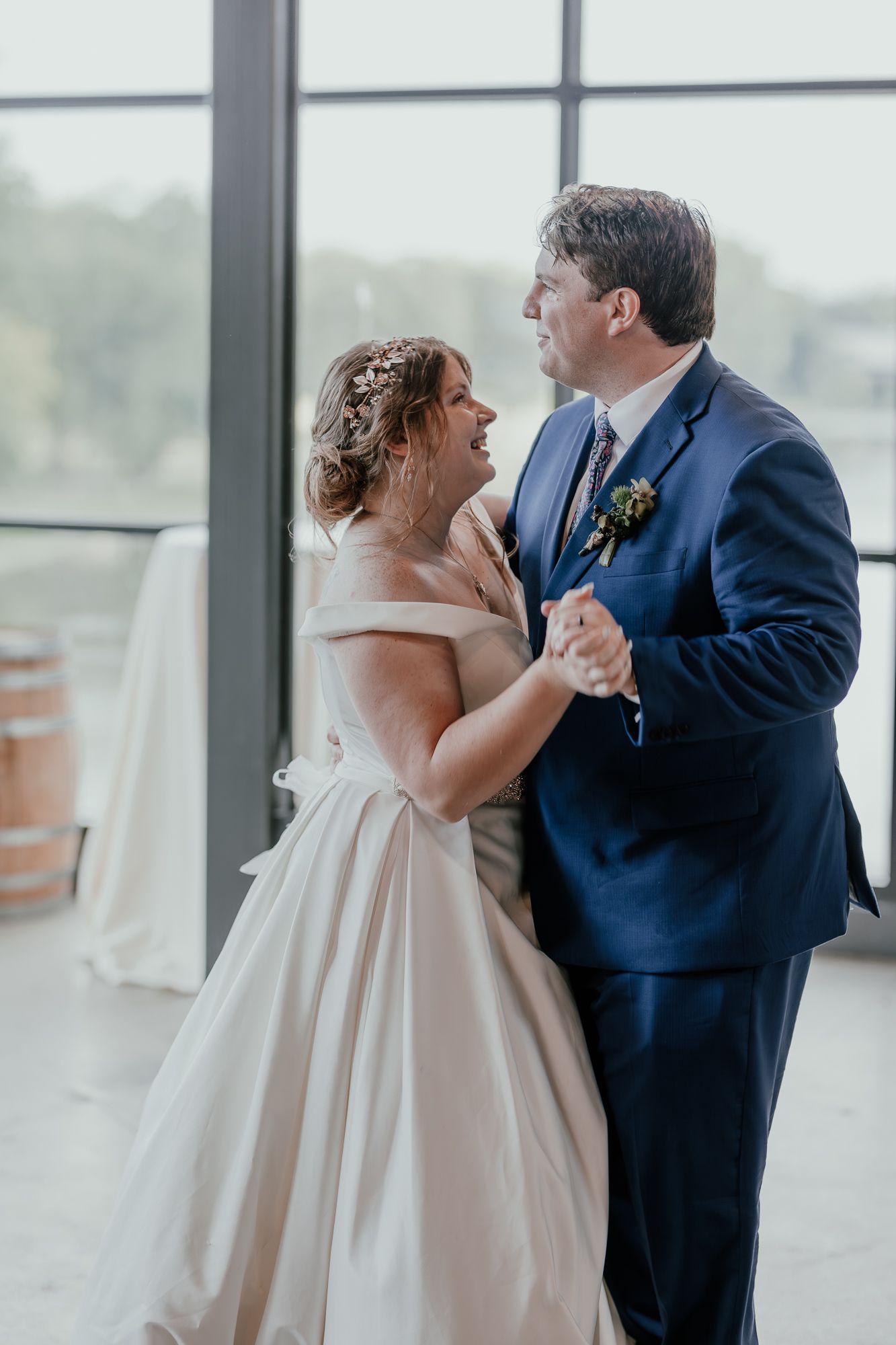 Couple dances together in elegant attire near large windows in modern venue.