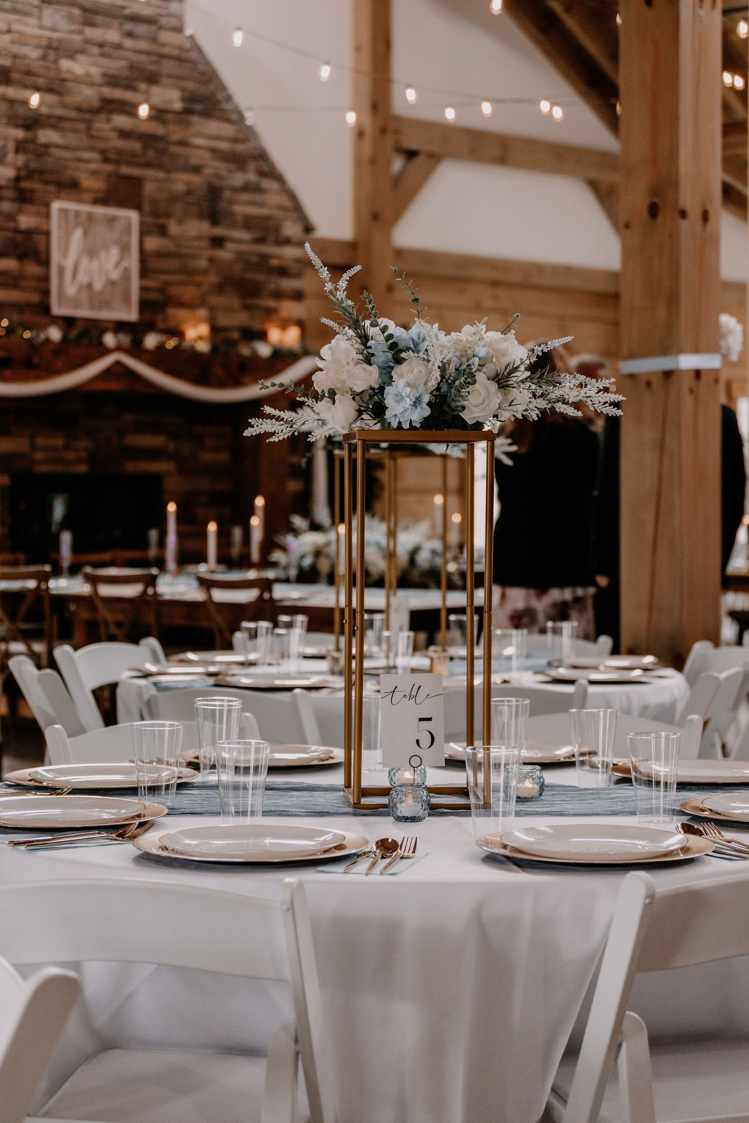 Modern wedding reception table setting with tall gold centerpiece and white floral arrangements.