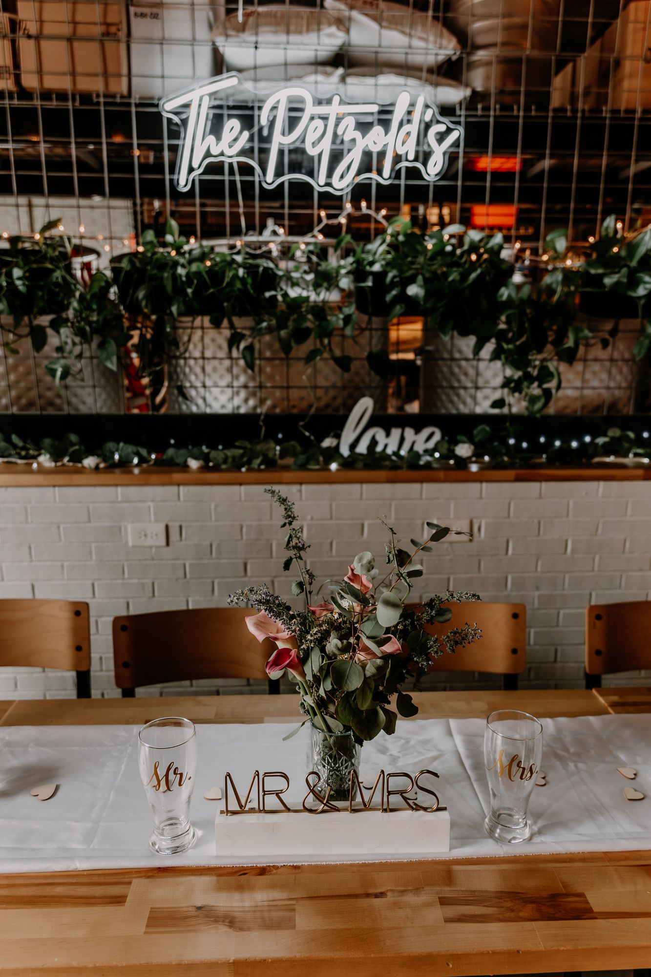 Wedding reception table with Mr & Mrs sign under neon lights and hanging greenery.