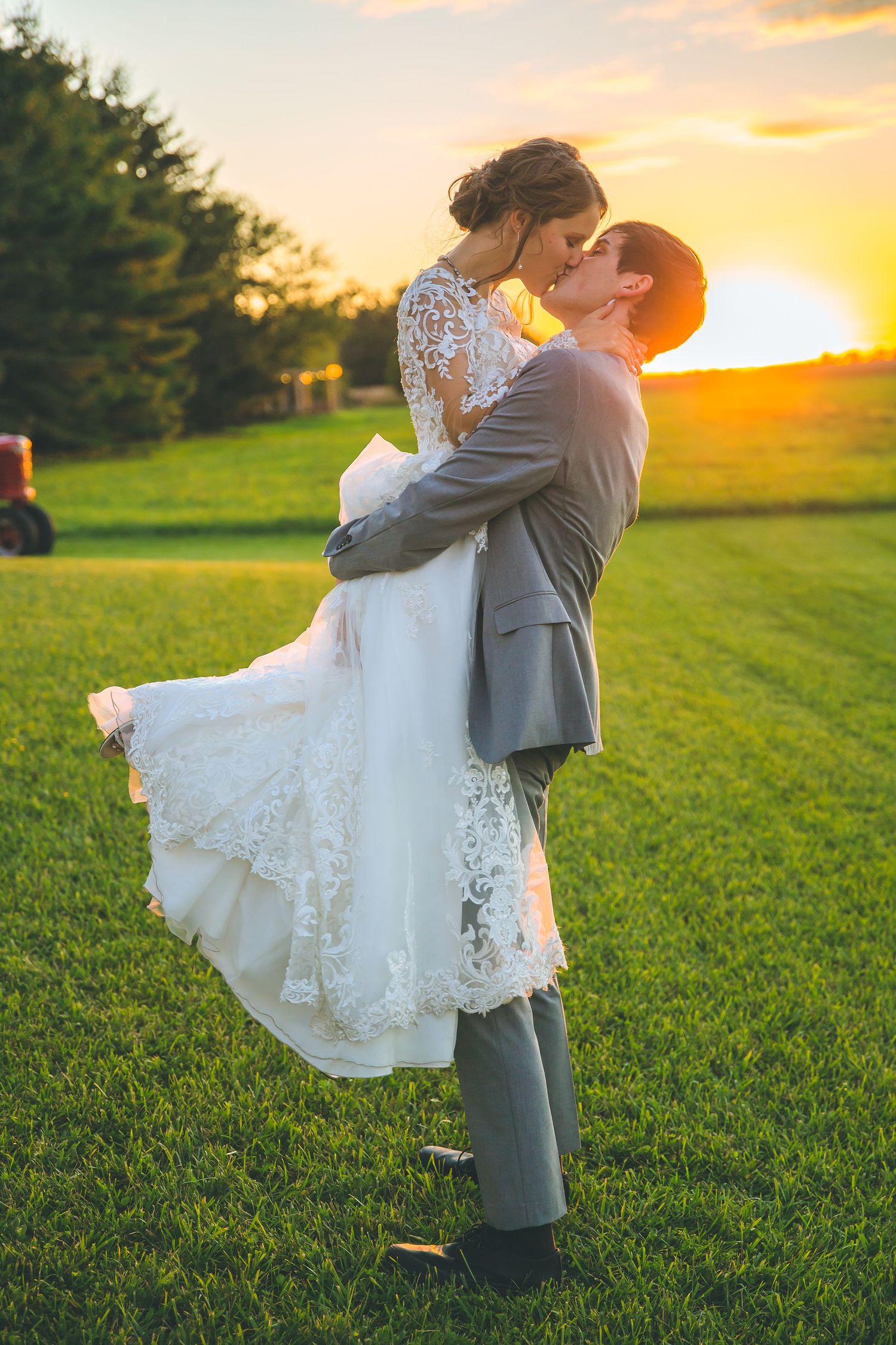 Newlyweds share an intimate moment during golden hour in a lush green field.
