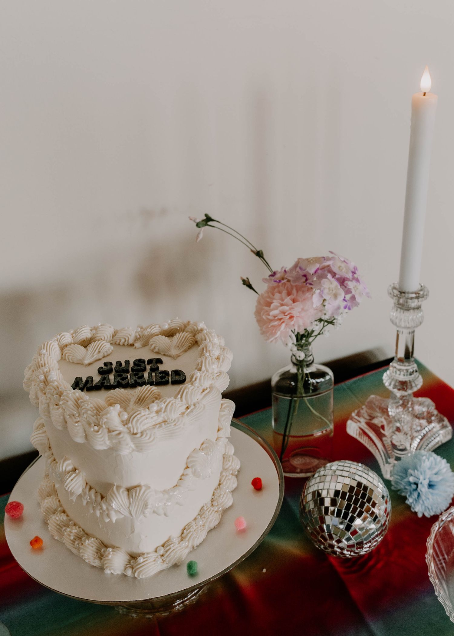White wedding cake with delicate piping decorations next to candle and disco ball on decorated table.