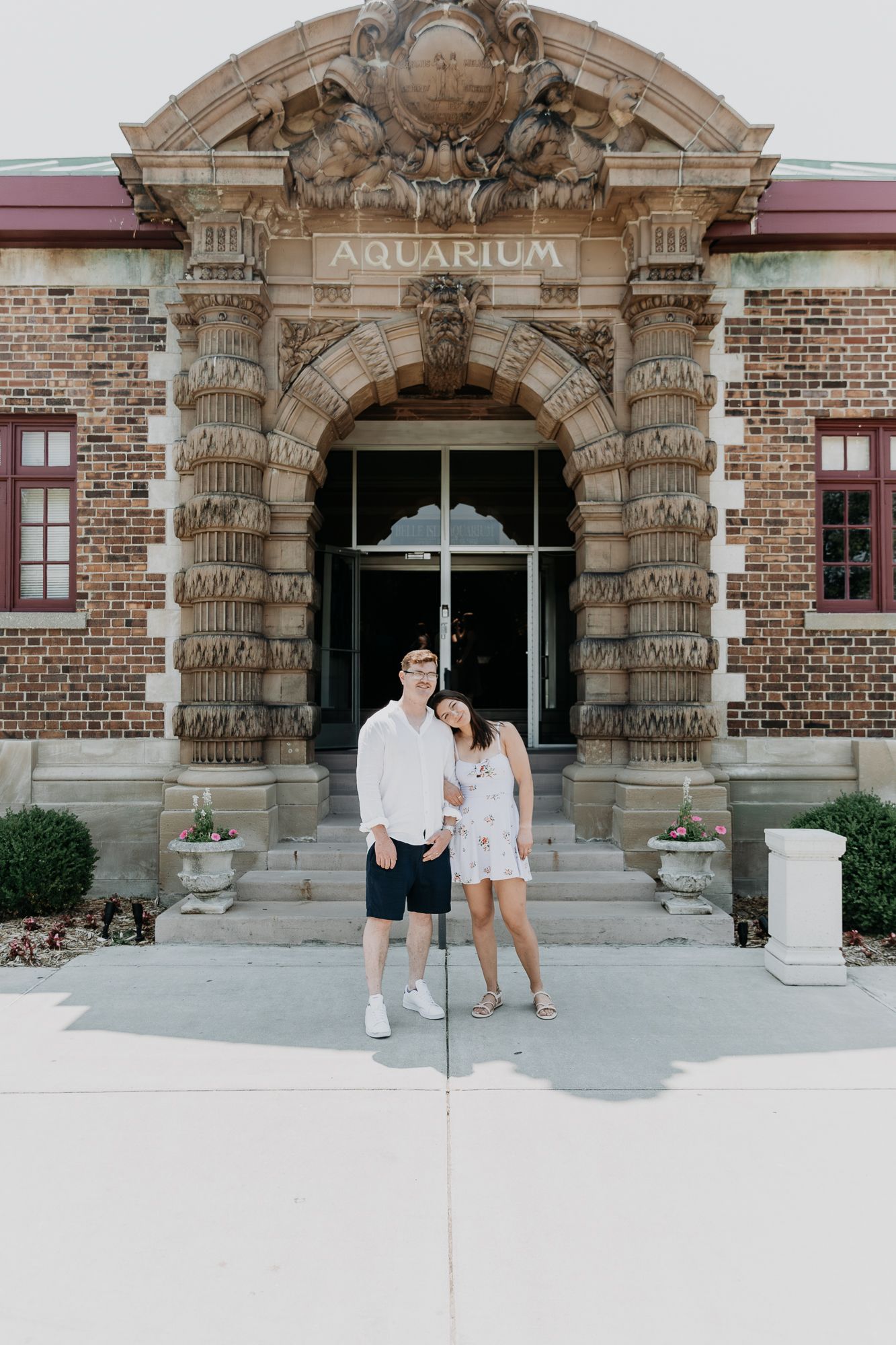A couple shares a romantic moment in front of an ornate stone archway entrance of a historic building.