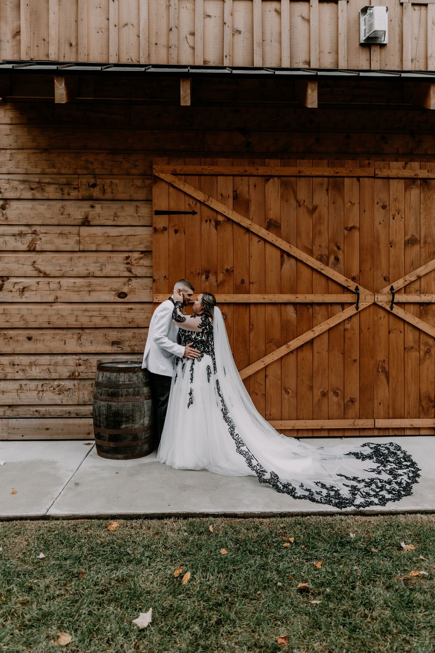 Newlyweds share an intimate moment against rustic barn door with bride's dramatic black and white lace train.