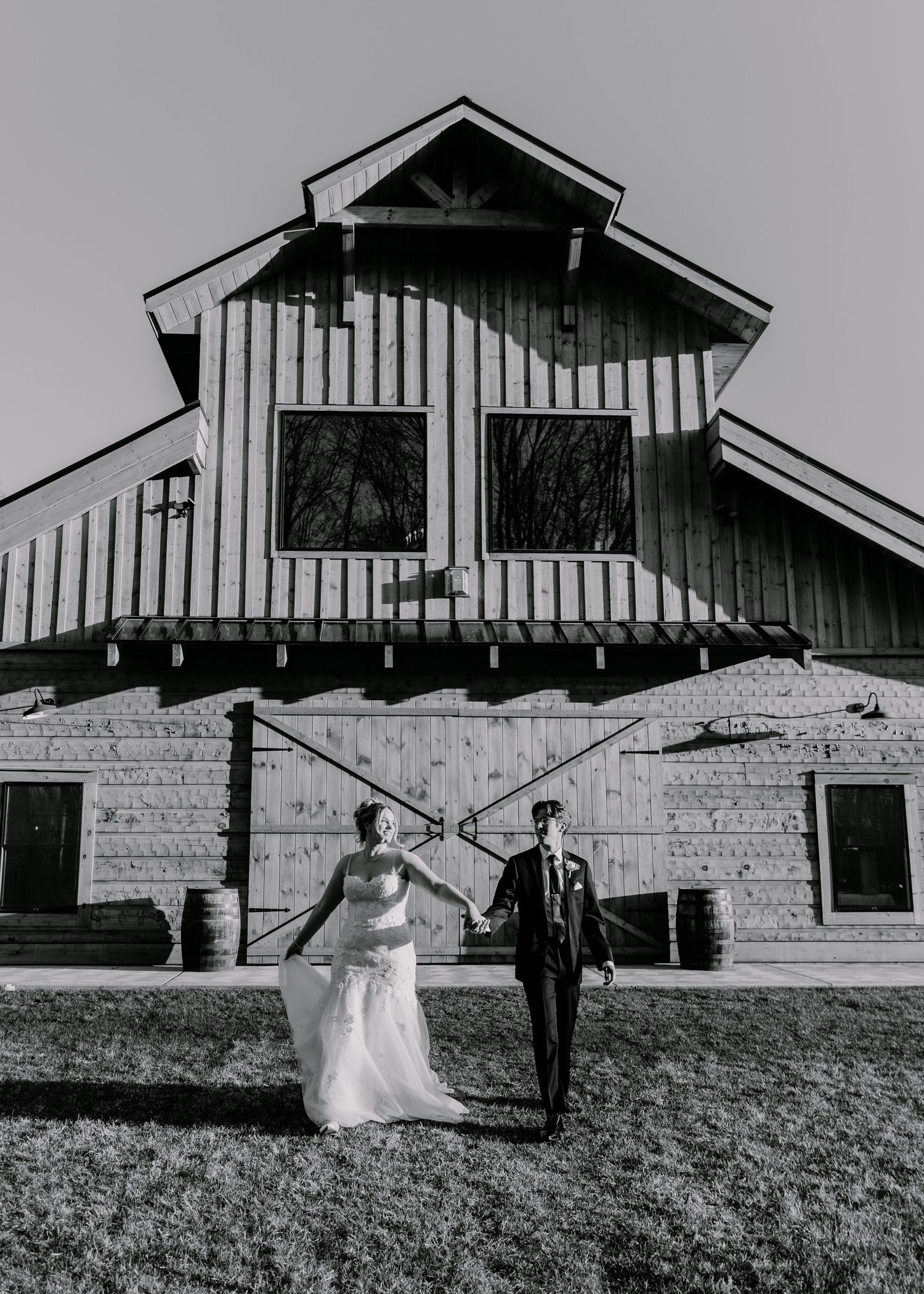 Newlyweds stand together in a black and white photo against a rustic barn exterior.