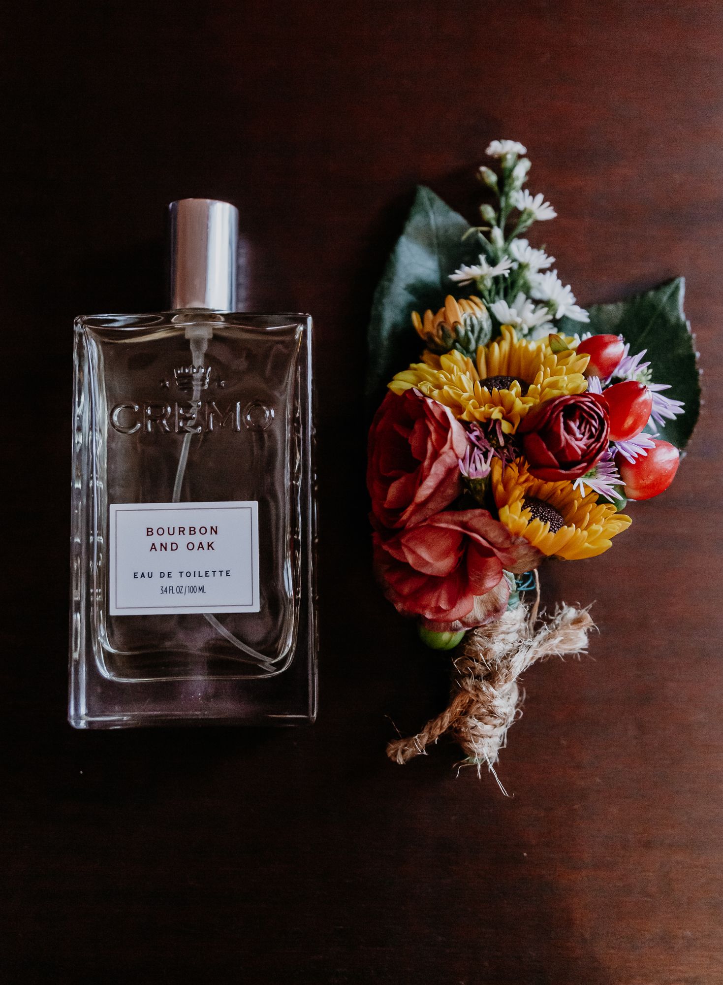 Wedding detail shot featuring perfume bottles and colorful floral arrangements on dark wood surface.
