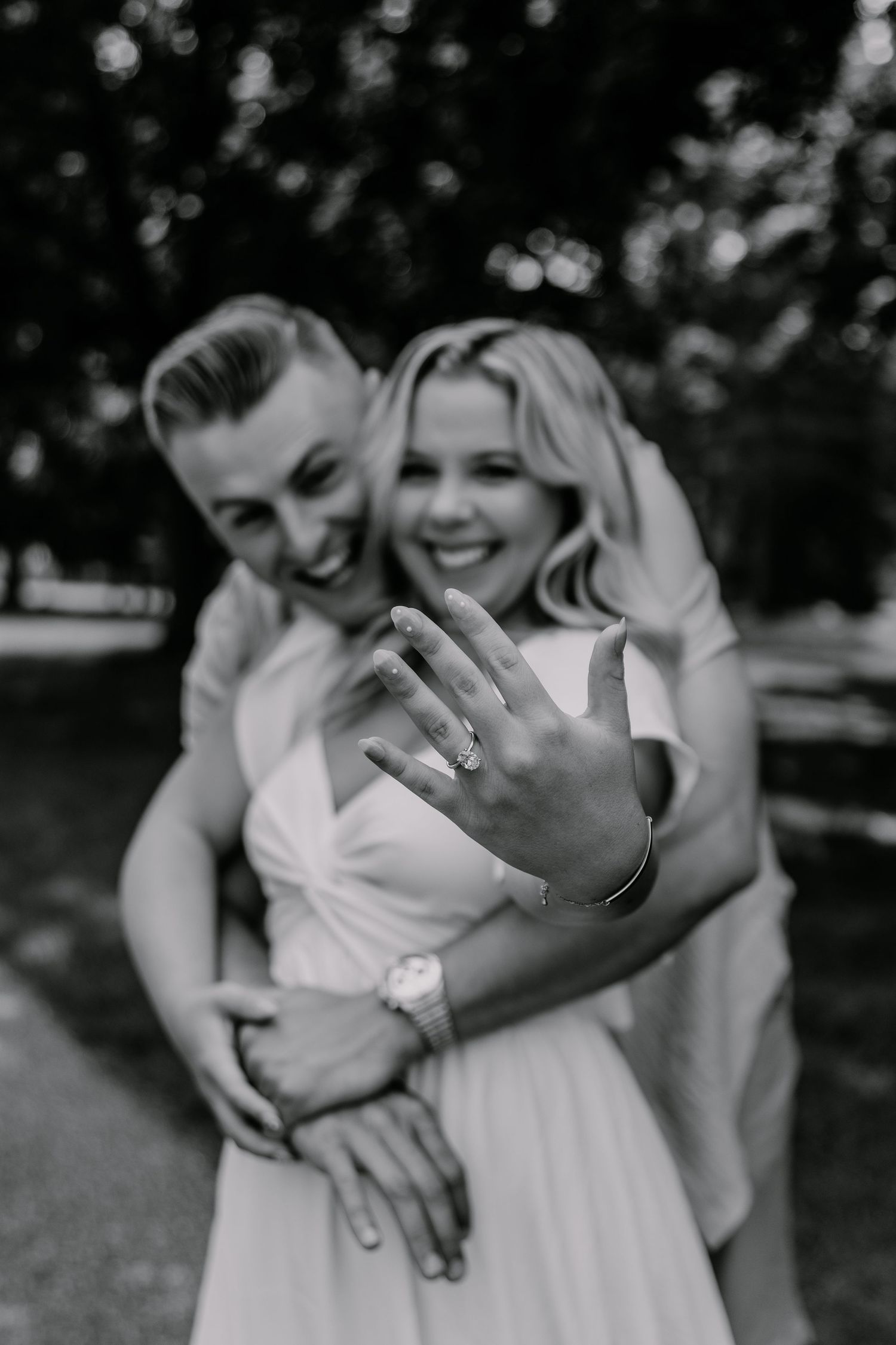 A series of black and white engagement photos showing a couple embracing outdoors in candid romantic poses.