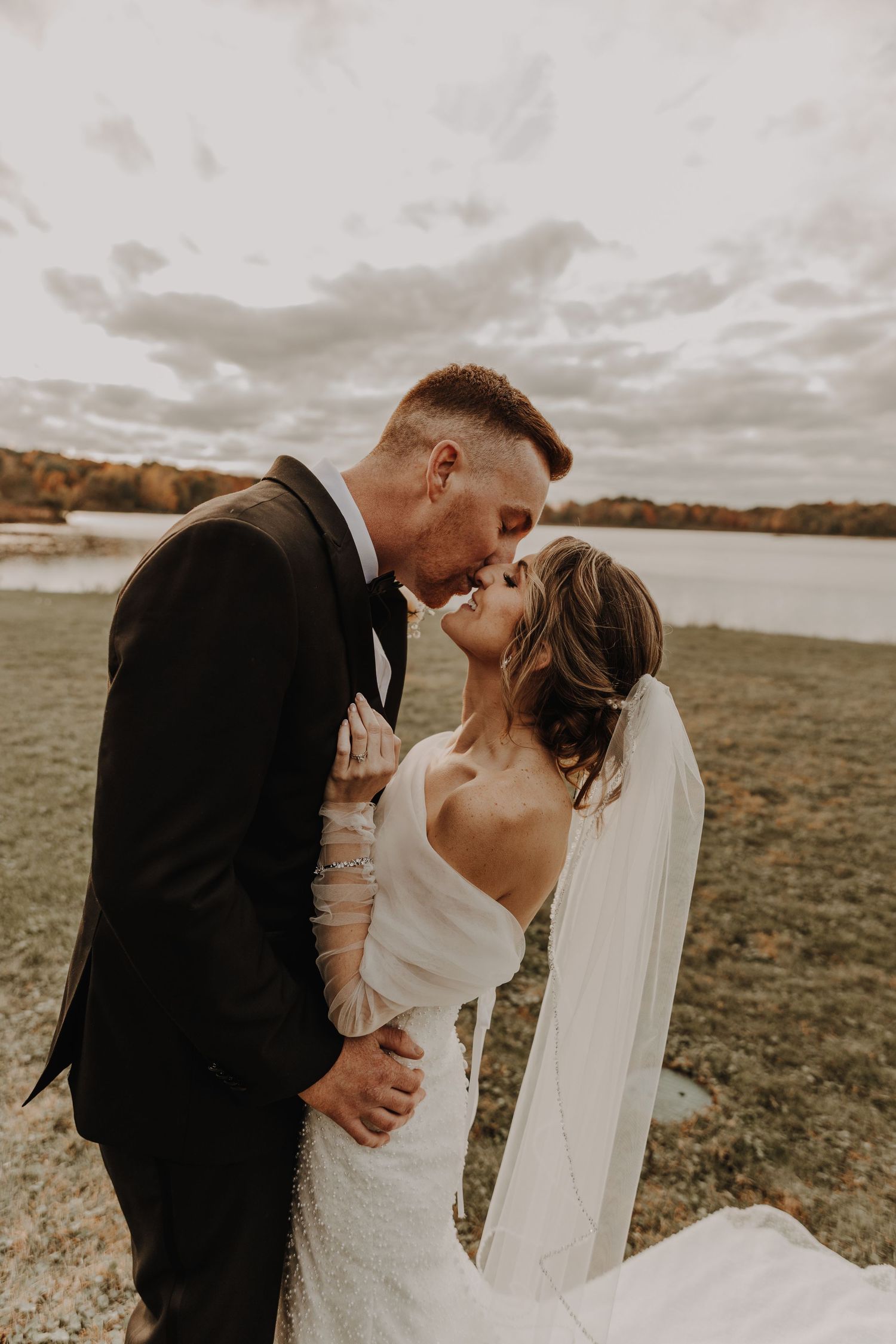 A romantic wedding photo series showing tender moments between newlyweds in a scenic outdoor field at sunset.