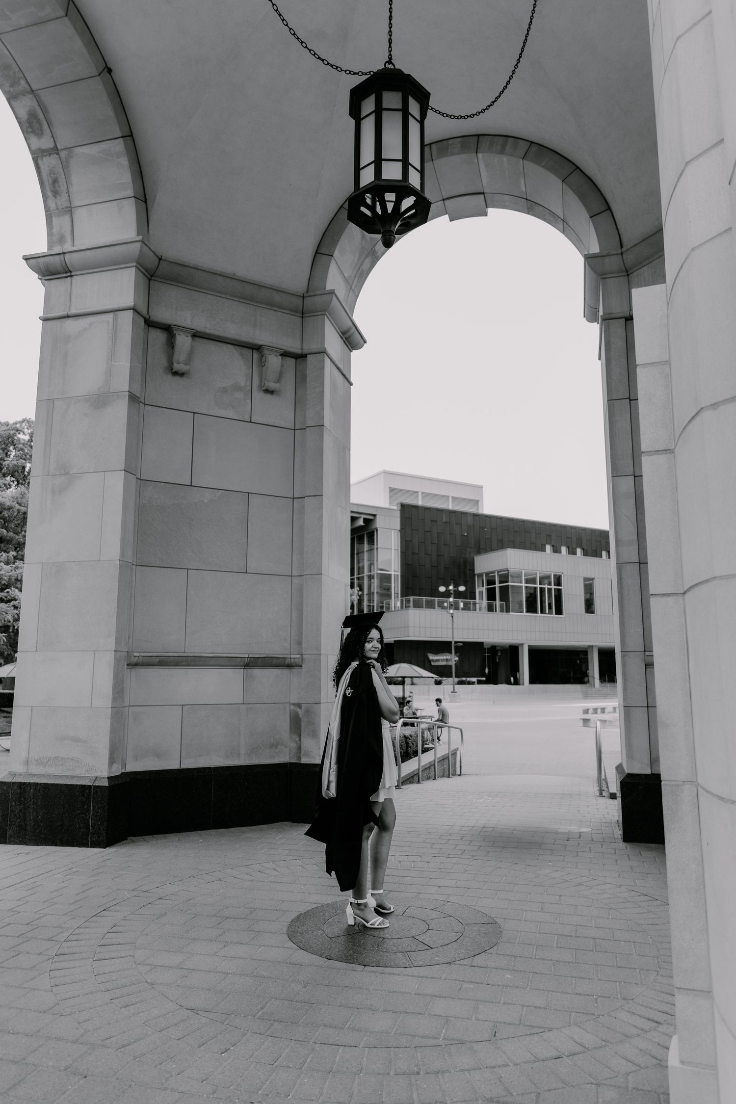 A figure stands under white arched pillars and columns in a minimalist building interior, captured in black and white.
