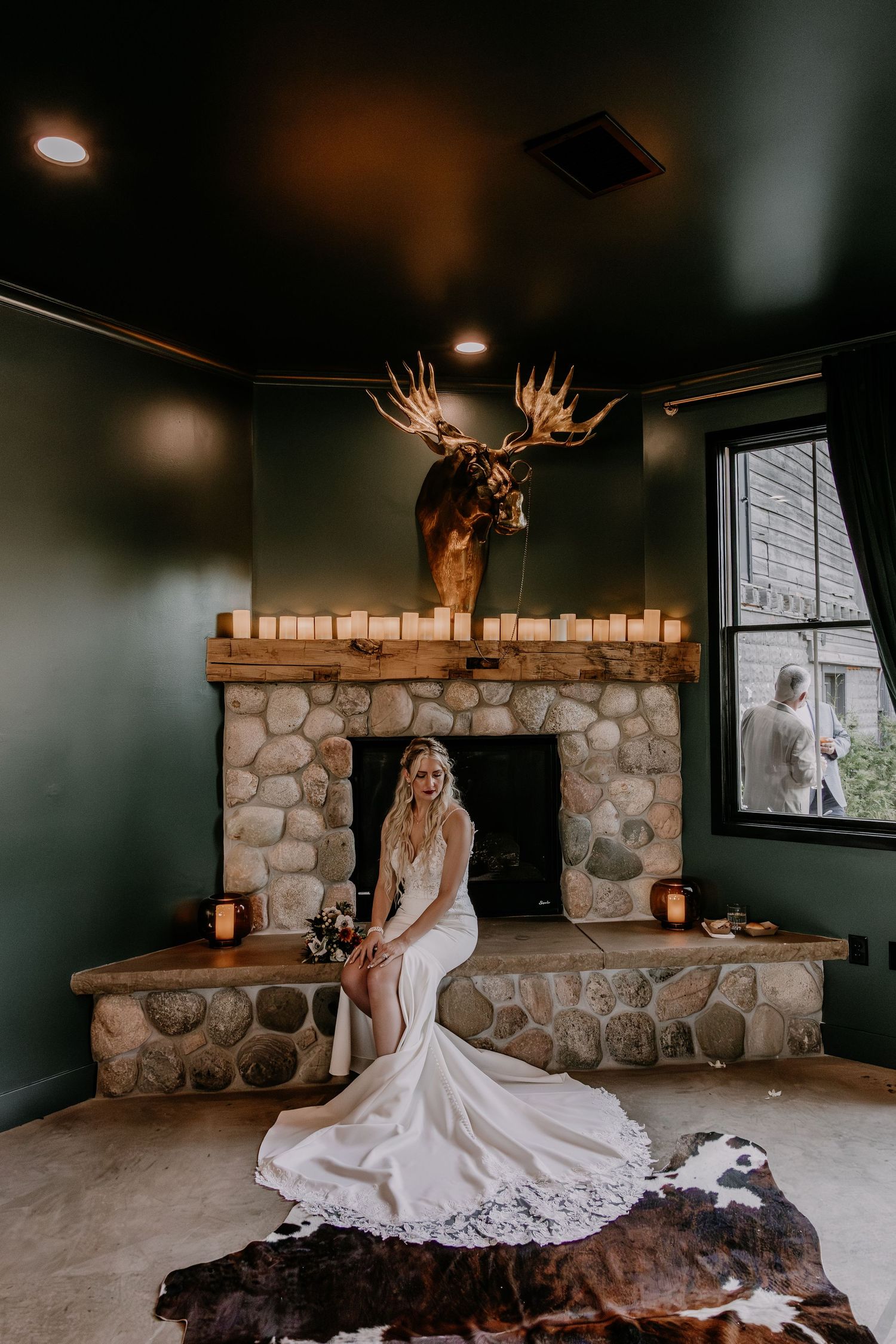Wedding dress displayed in a rustic room with stone walls and mounted deer antlers creating dramatic ambiance.
