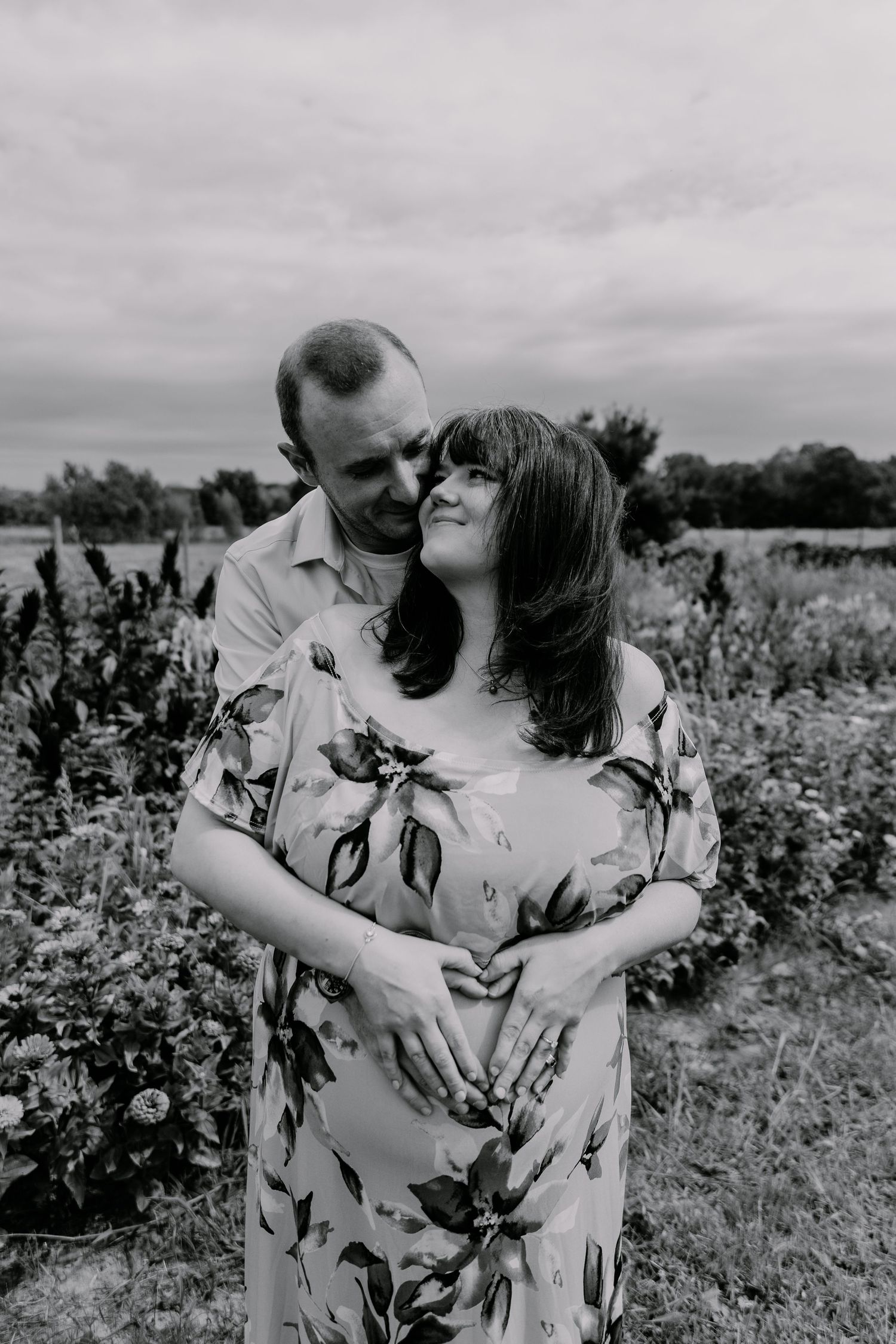 A romantic black and white portrait of an intimate moment between a couple embracing in a flower field.