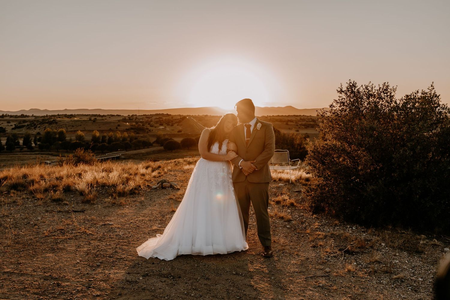 Wedding couple poses together in a desert landscape at golden hour with dramatic lighting and mountains in background.