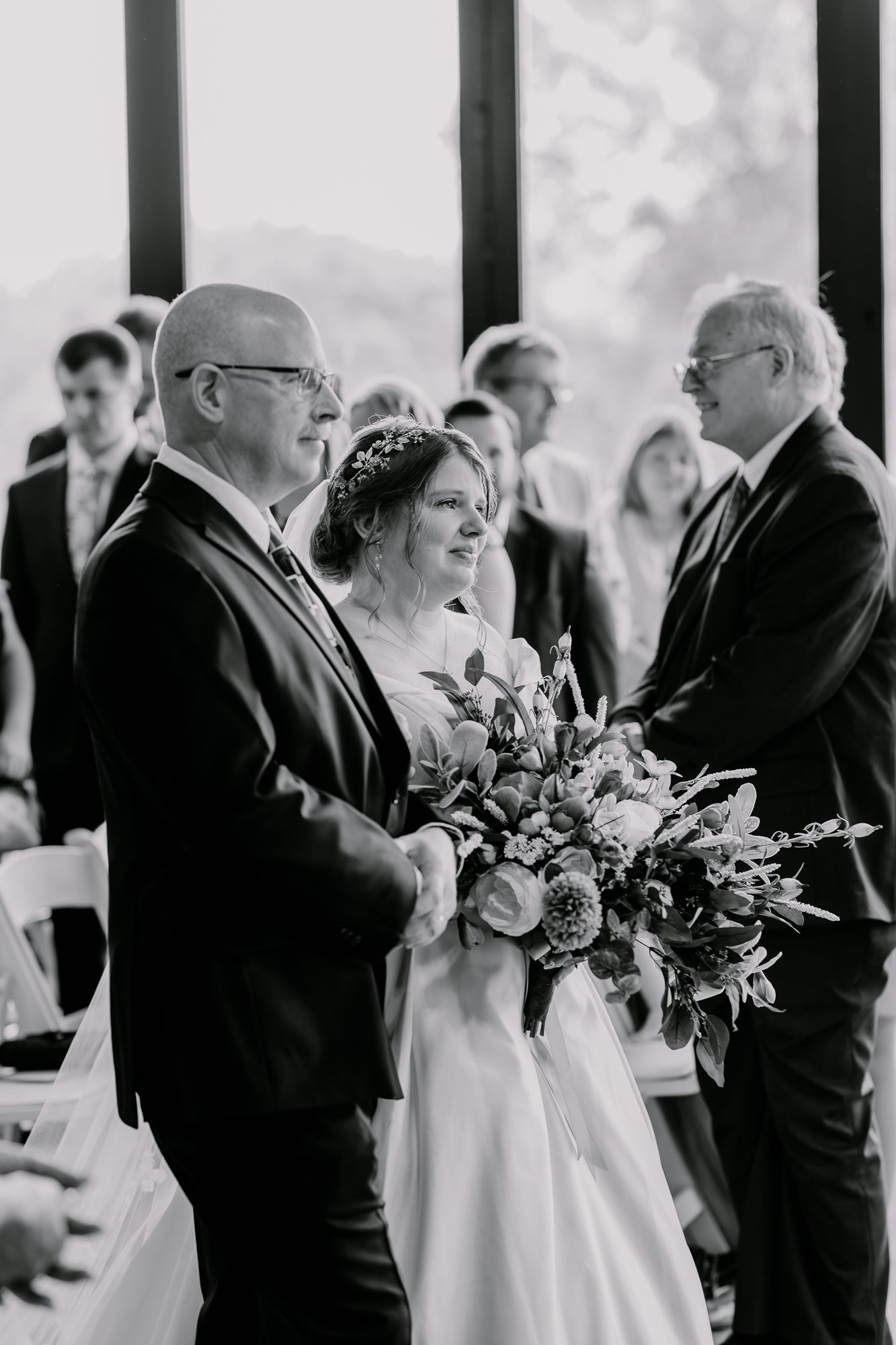 Black and white wedding ceremony moment with attendees gathered in natural light venue.