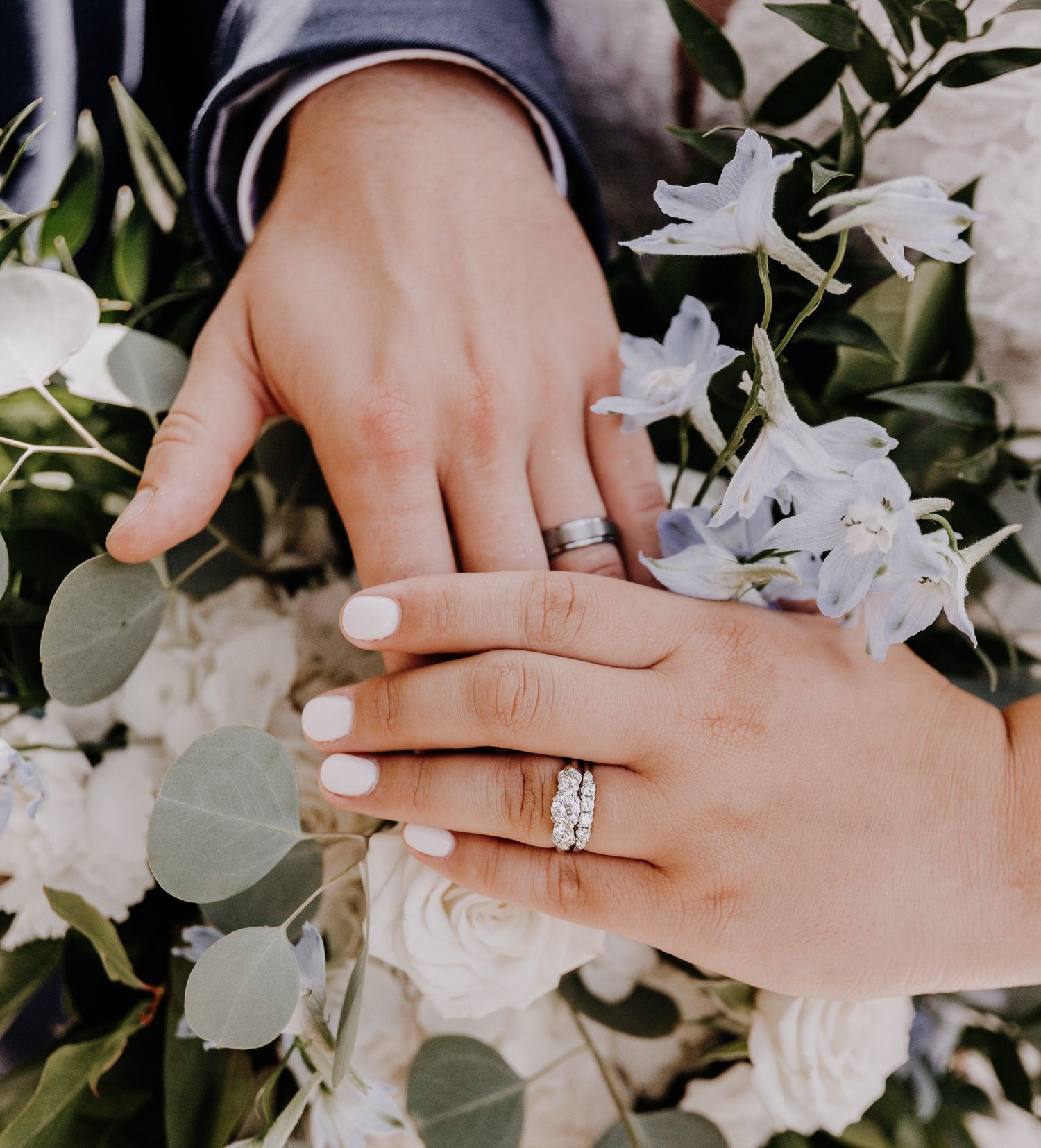 Wedding rings sparkle against white flowers and eucalyptus leaves in romantic detail shot.