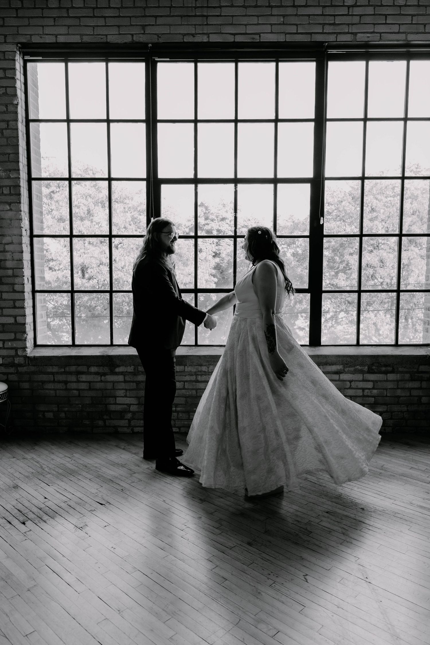 A romantic black and white portrait of a couple dancing in front of bright windows.