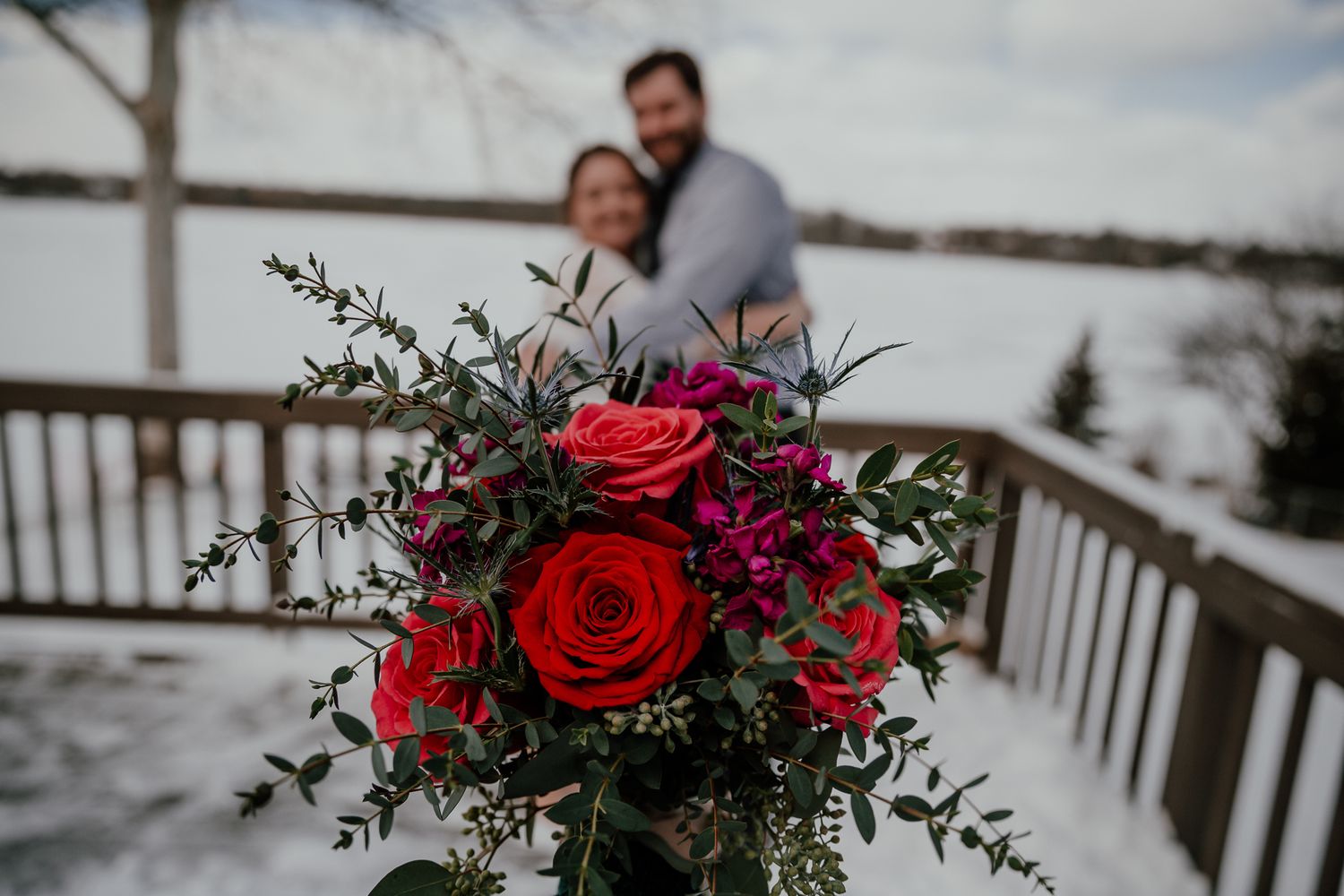 Wedding bouquet with vibrant red roses and greenery against a snowy winter backdrop.