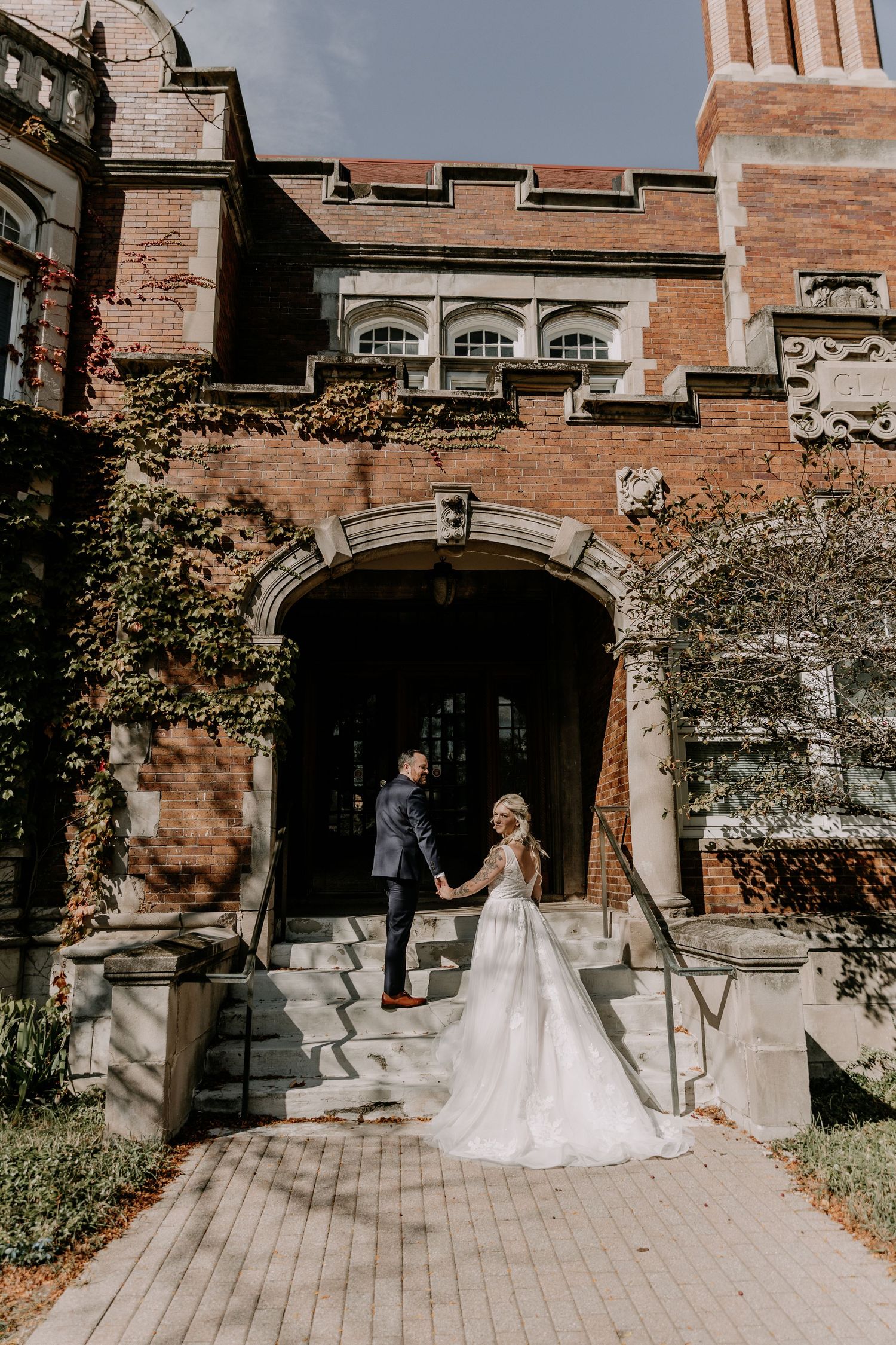 A romantic first look moment unfolds outside a grand stone building with arched doorways.