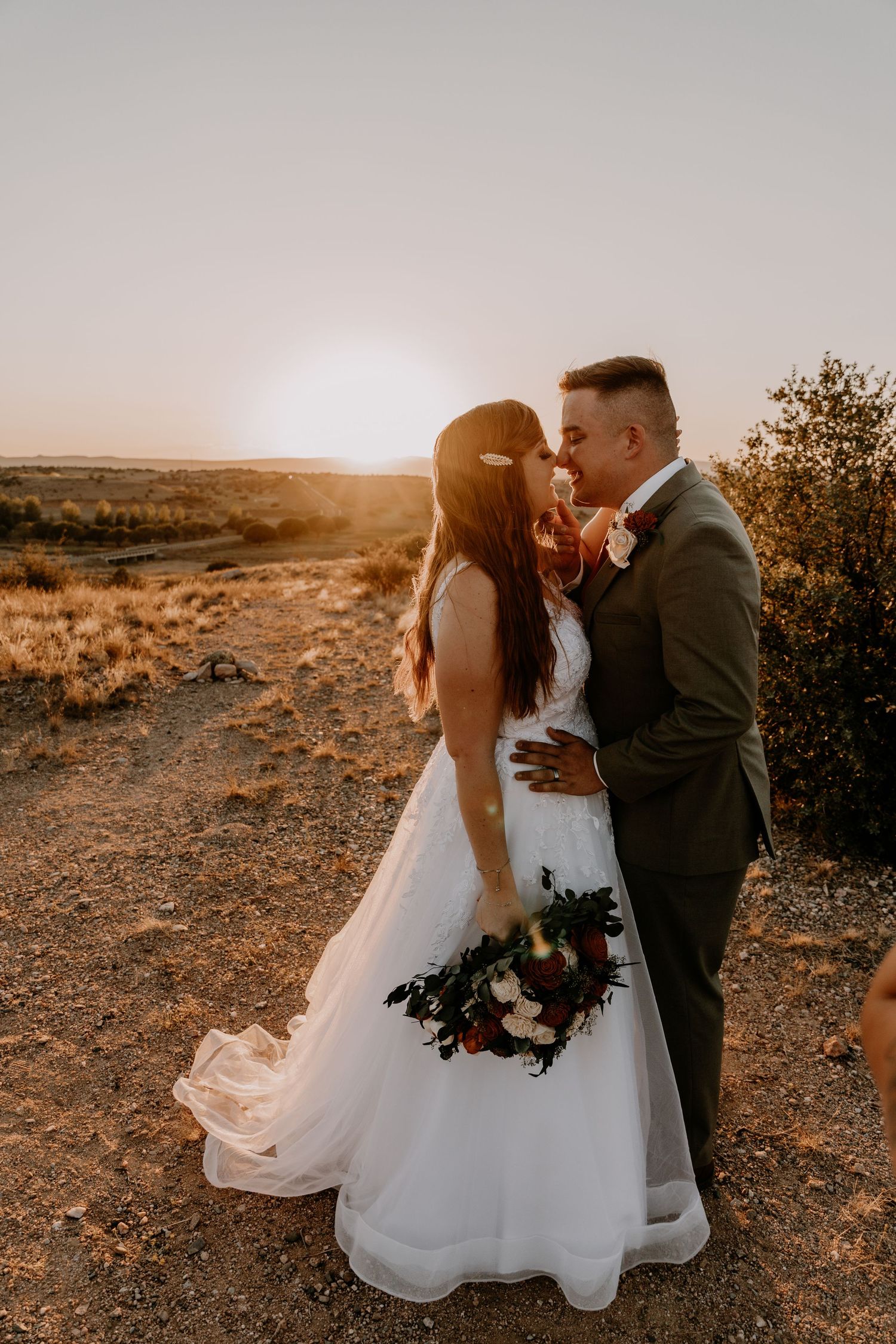 Wedding couple embraces during golden hour in a desert setting with flowing white dress.
